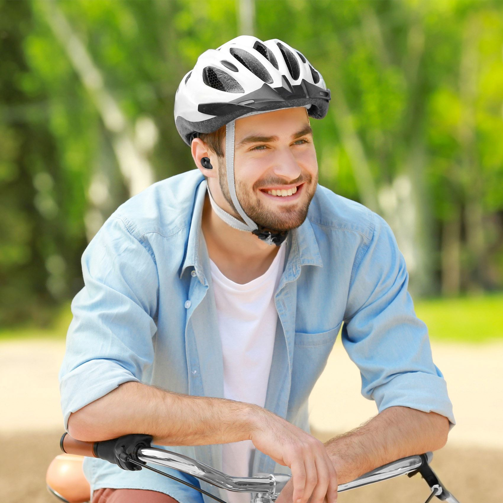 Uomo in bicicletta, con casco e auricolari. Sorride. Sfondo verde.