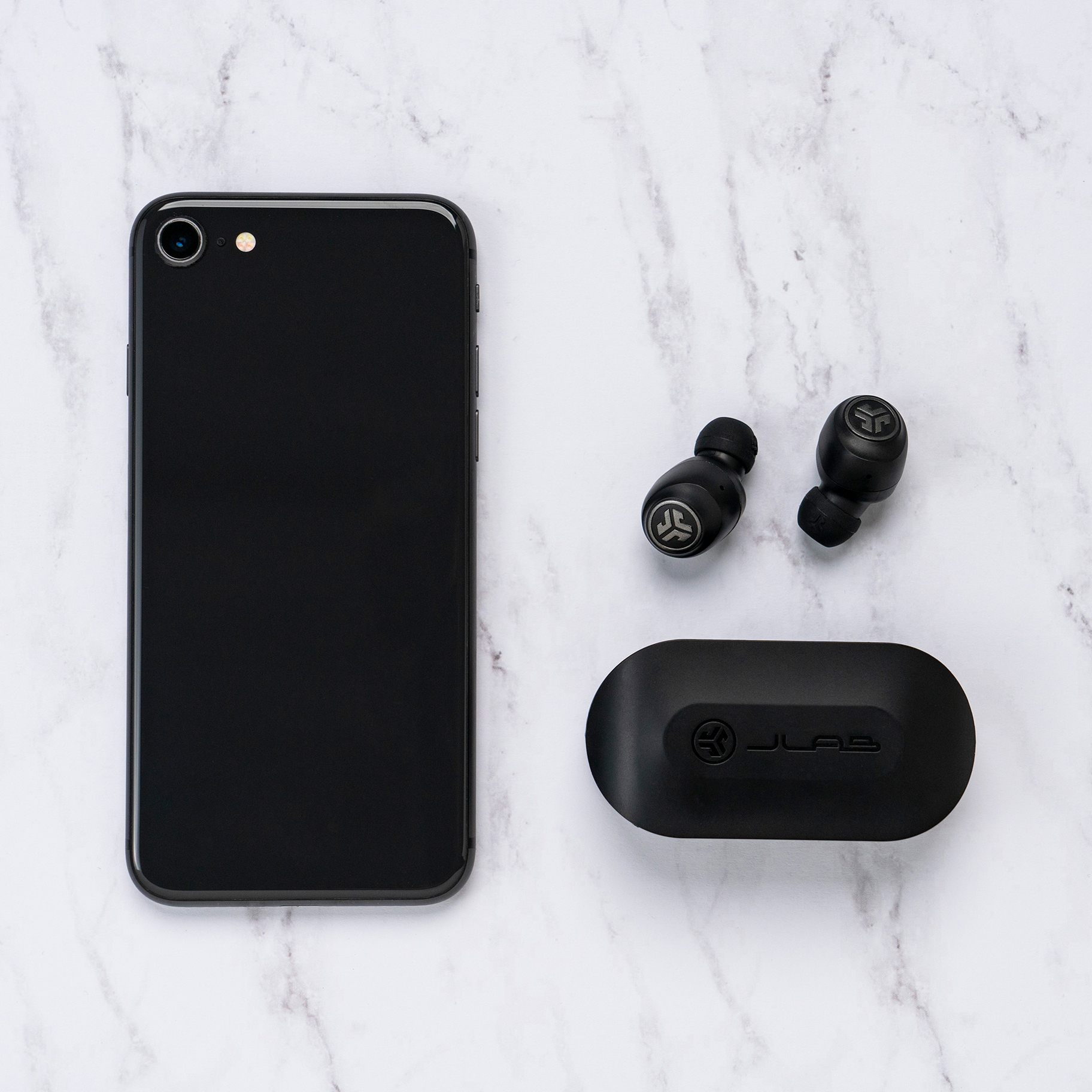 Schwarzes Telefon, Ohrhörer und Ladecase auf Marmor. Ohrhörer und Case sind schwarz, Telefon hat eine Kamera.