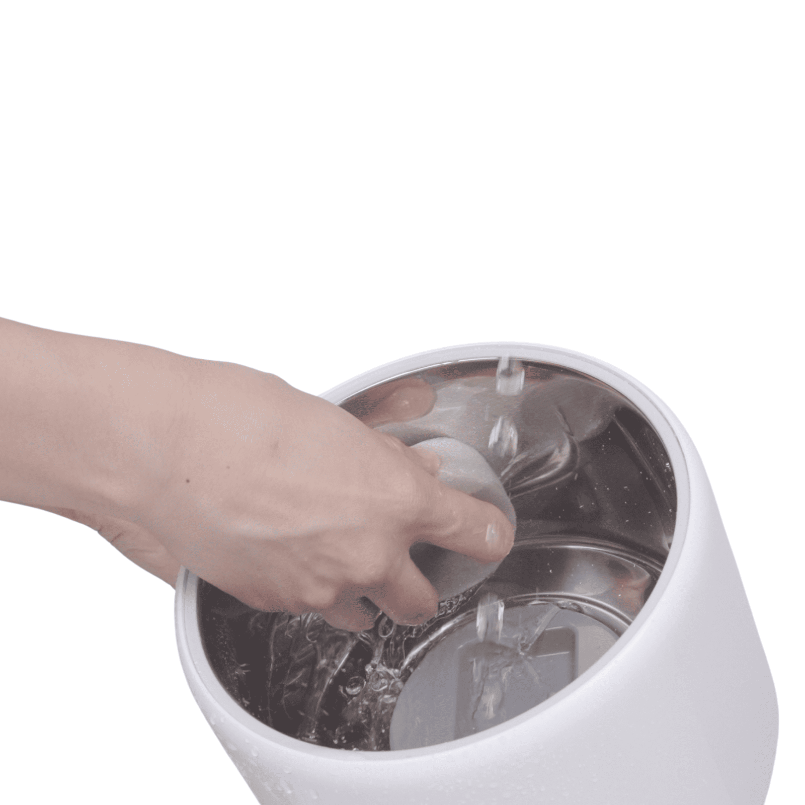 Hand, die einen felsenartigen Gegenstand in einen weißen, metallischen Behälter mit Wasser taucht.