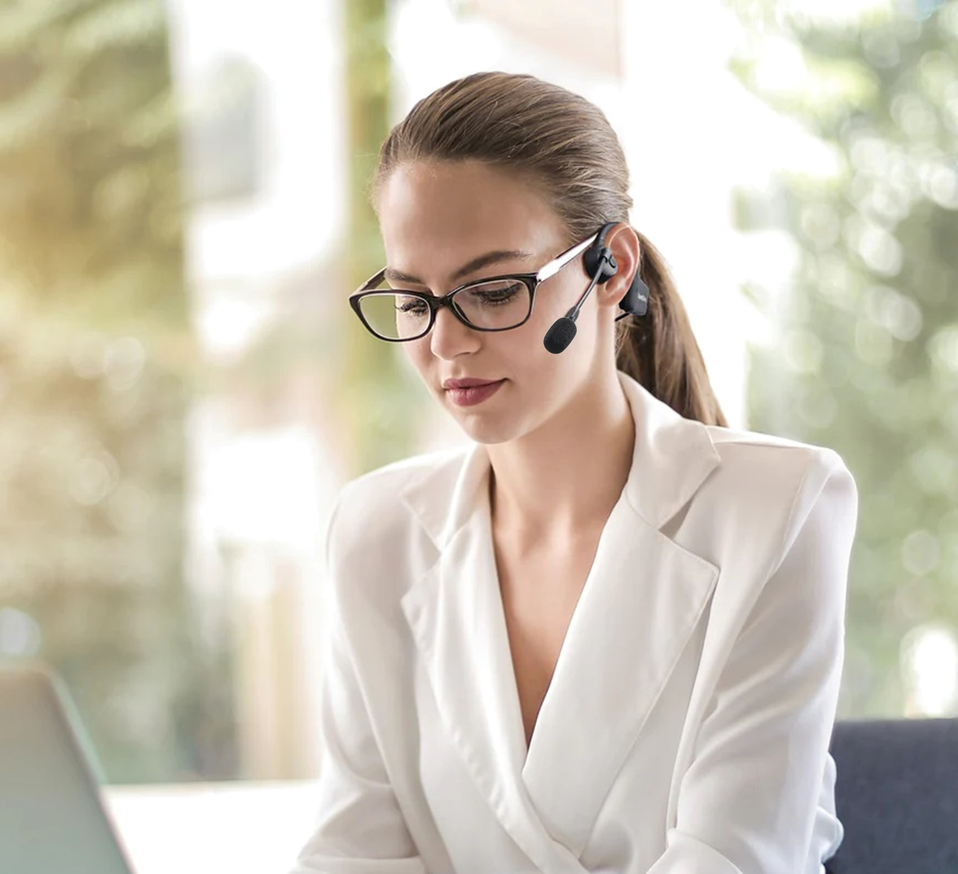 Una donna con occhiali e cuffie, che lavora su un laptop in un ambiente ufficio.