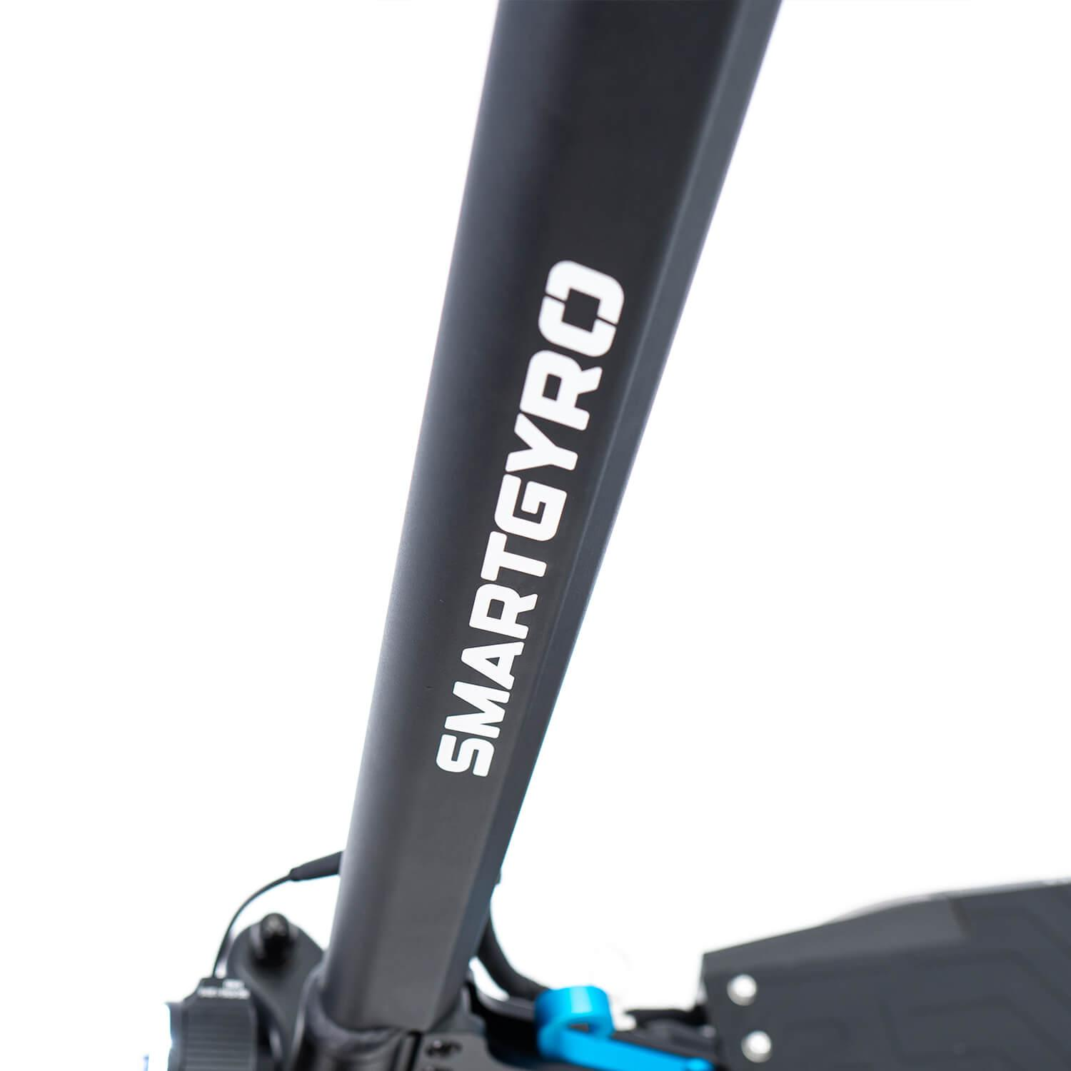 Fragment czarnej hulajnogi pokazuje tekst 'SMARTGYRO'. Hulajnoga znajduje się na białym tle.