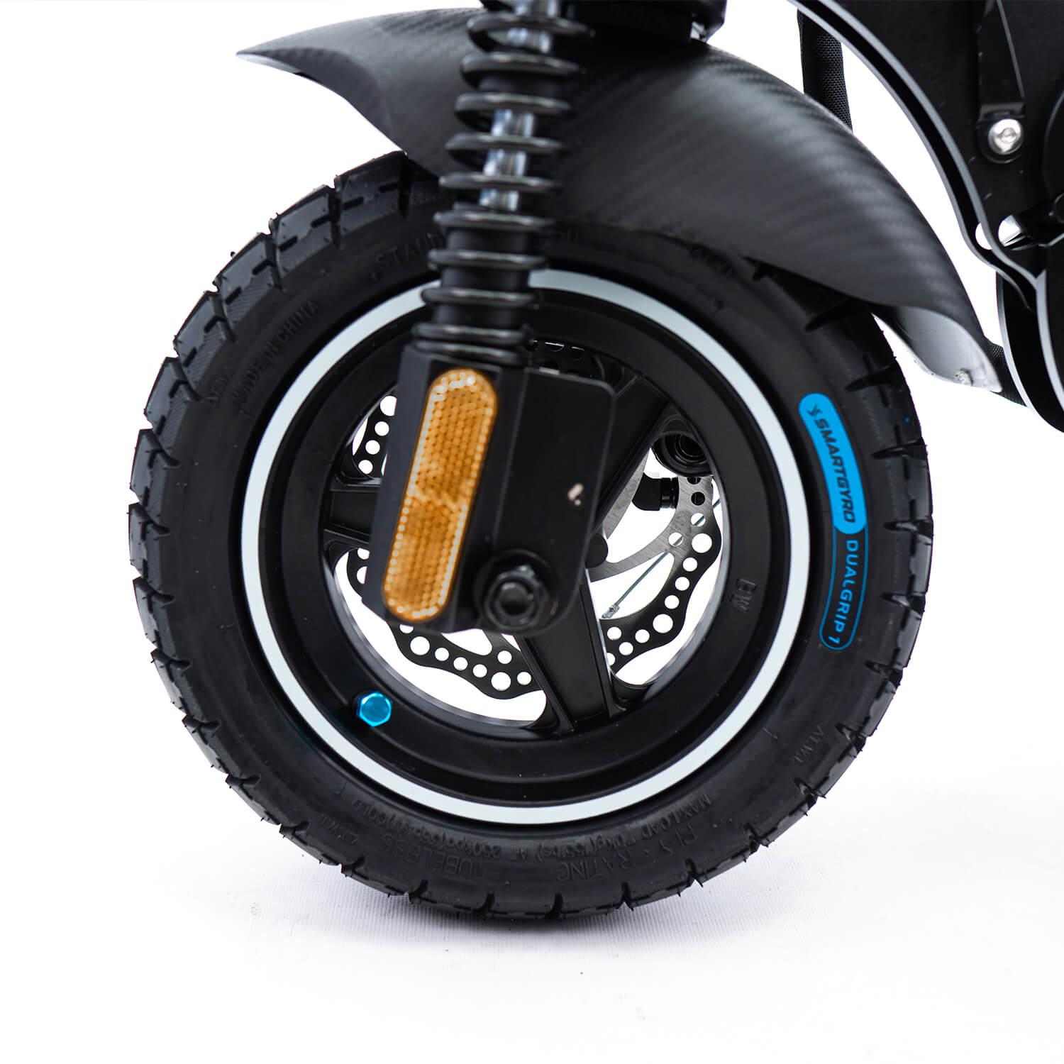 Zbliżenie czarnego koła skutera z oponą, białą obręczą i tarczami hamulcowymi.