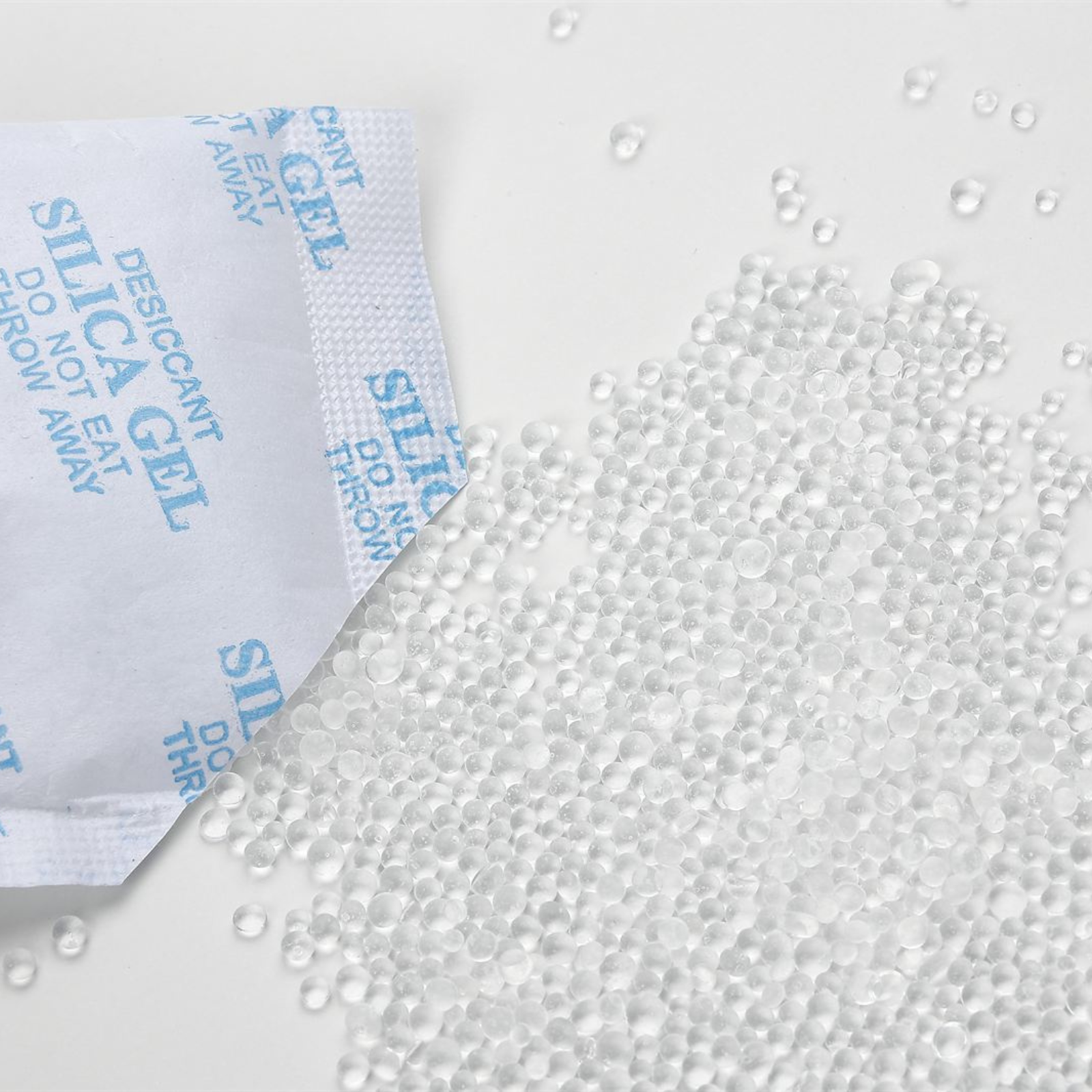 Silica-Gel-Beutel und klare Silica-Gel-Kügelchen, weißer Hintergrund.