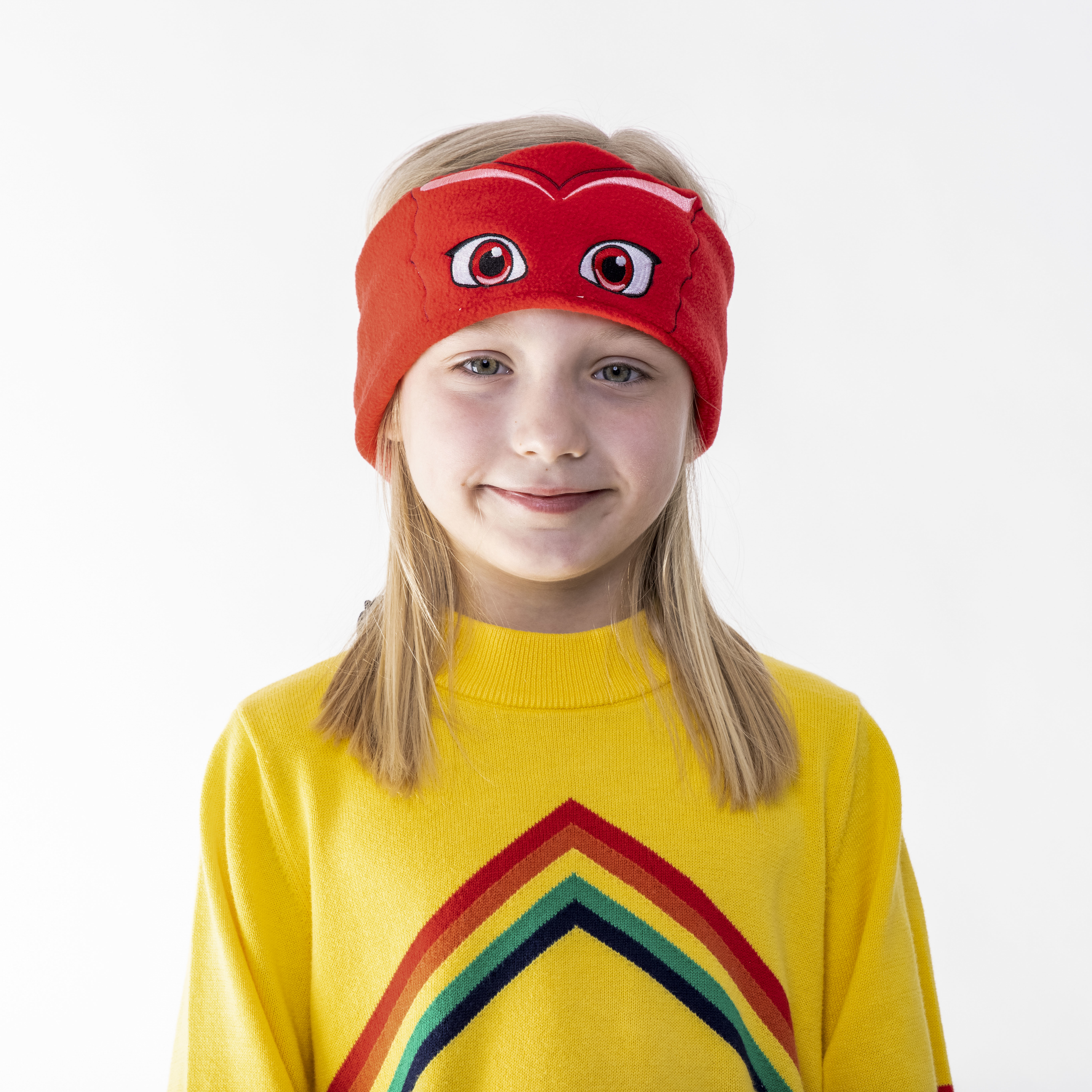 Junges Mädchen mit rotem Masken-Stirnband und gelbem Pullover mit Regenbogenmuster.
