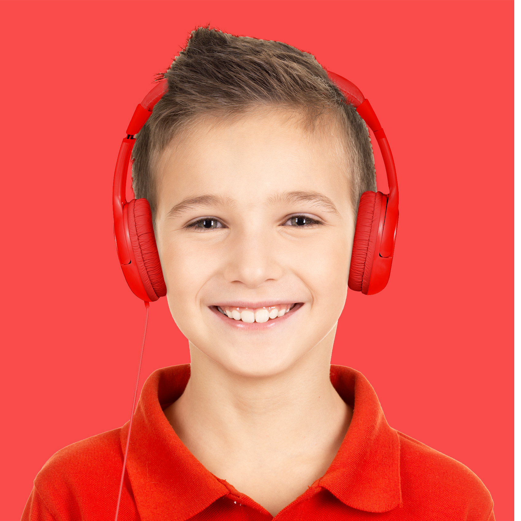 Mały chłopiec w czerwonych słuchawkach, uśmiechnięty do kamery na czerwonym tle.