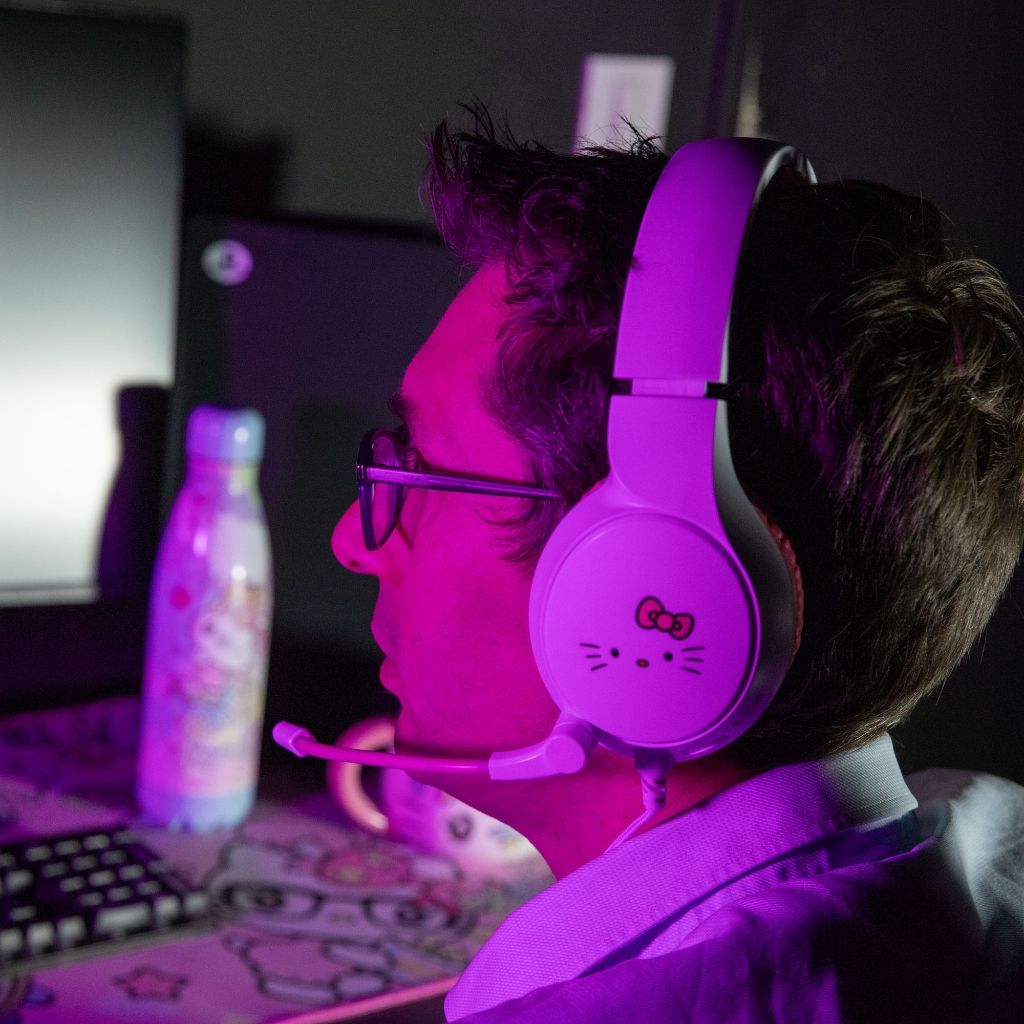 Mężczyzna w fioletowych słuchawkach Hello Kitty. Patrzy na ekran.