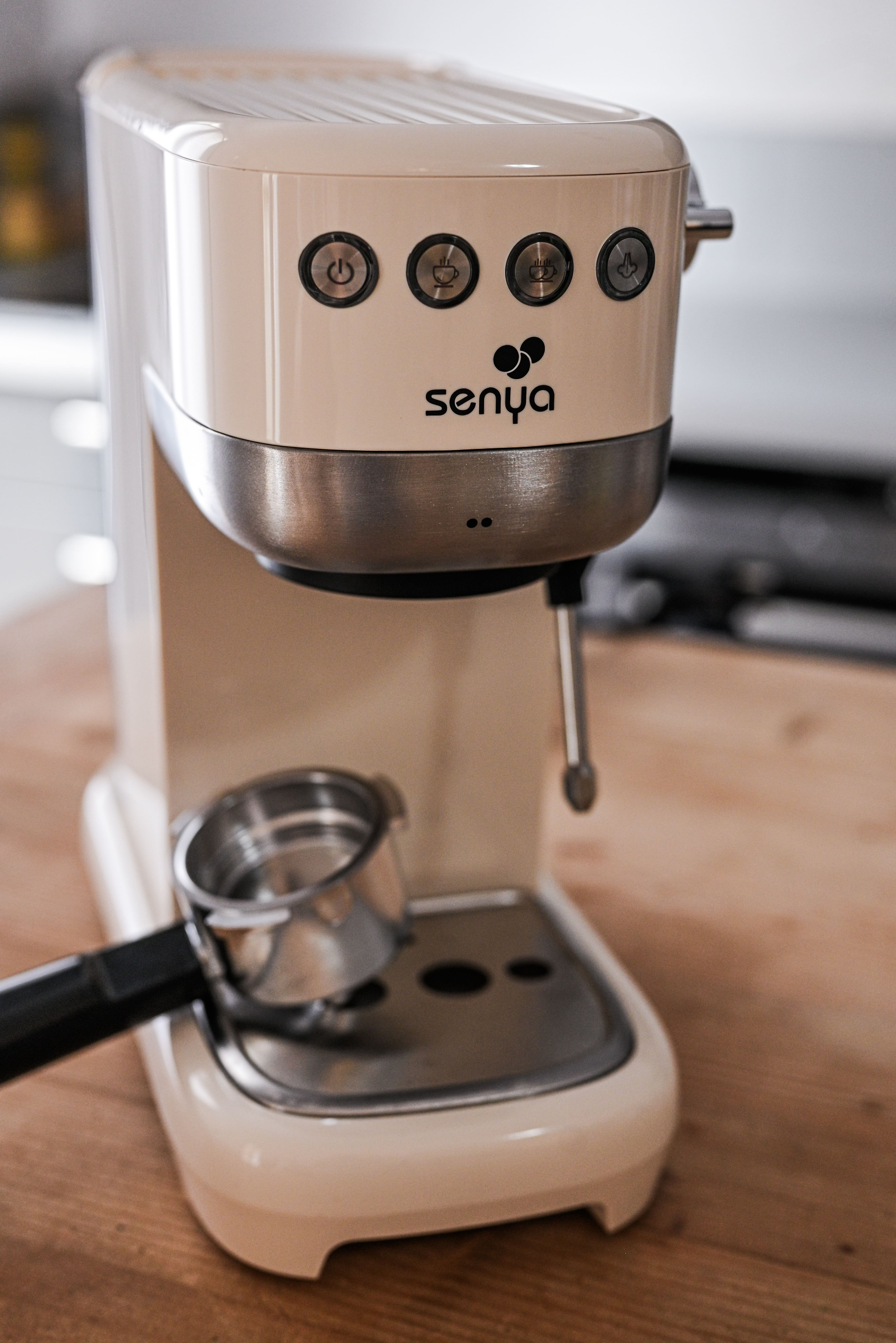 Cremefarbene Espressomaschine mit schwarzen Knöpfen und Senya-Logo. Ein Siebträger davor.