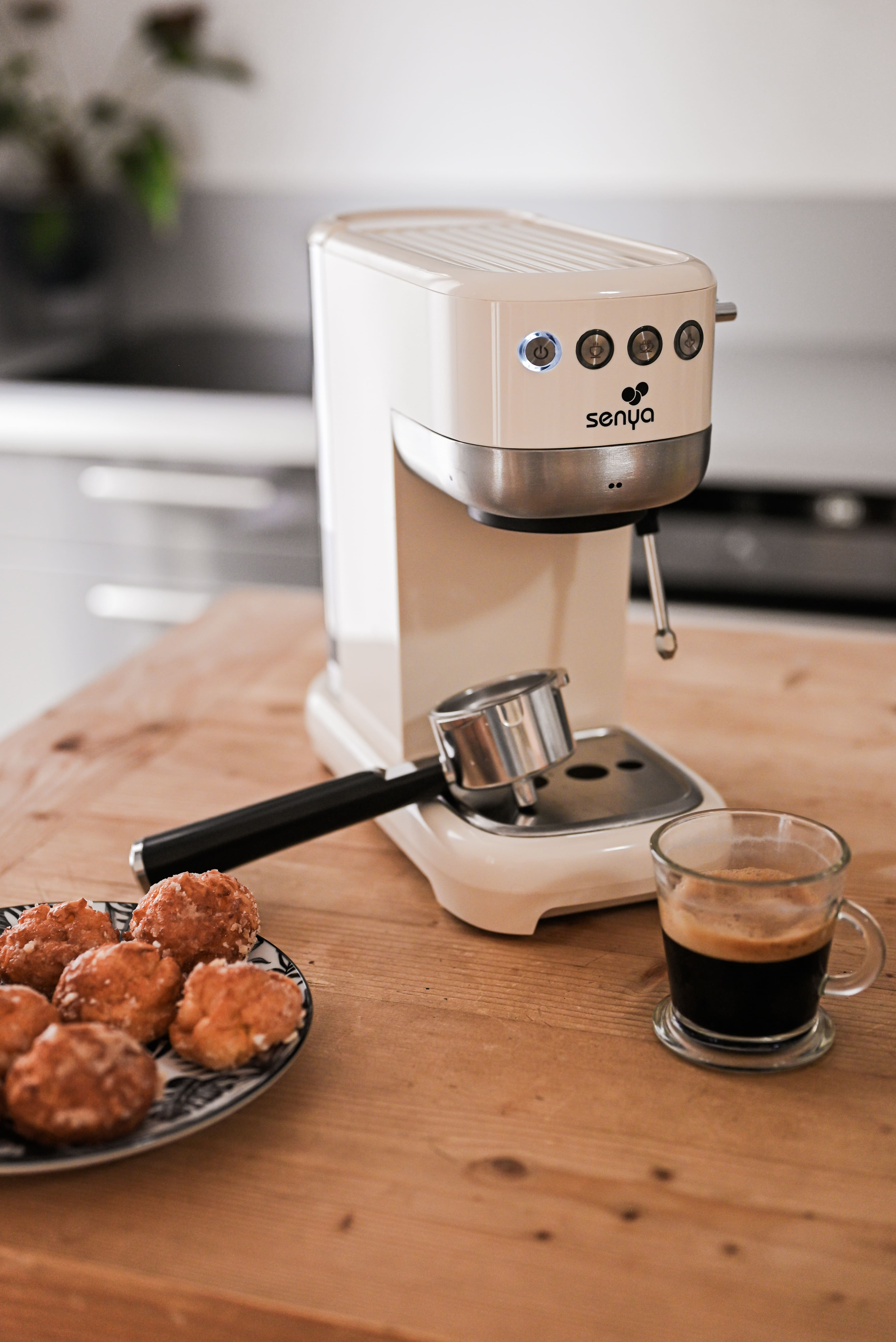 Espressomaschine mit einer Tasse Kaffee und Gebäck auf einem Holztisch.