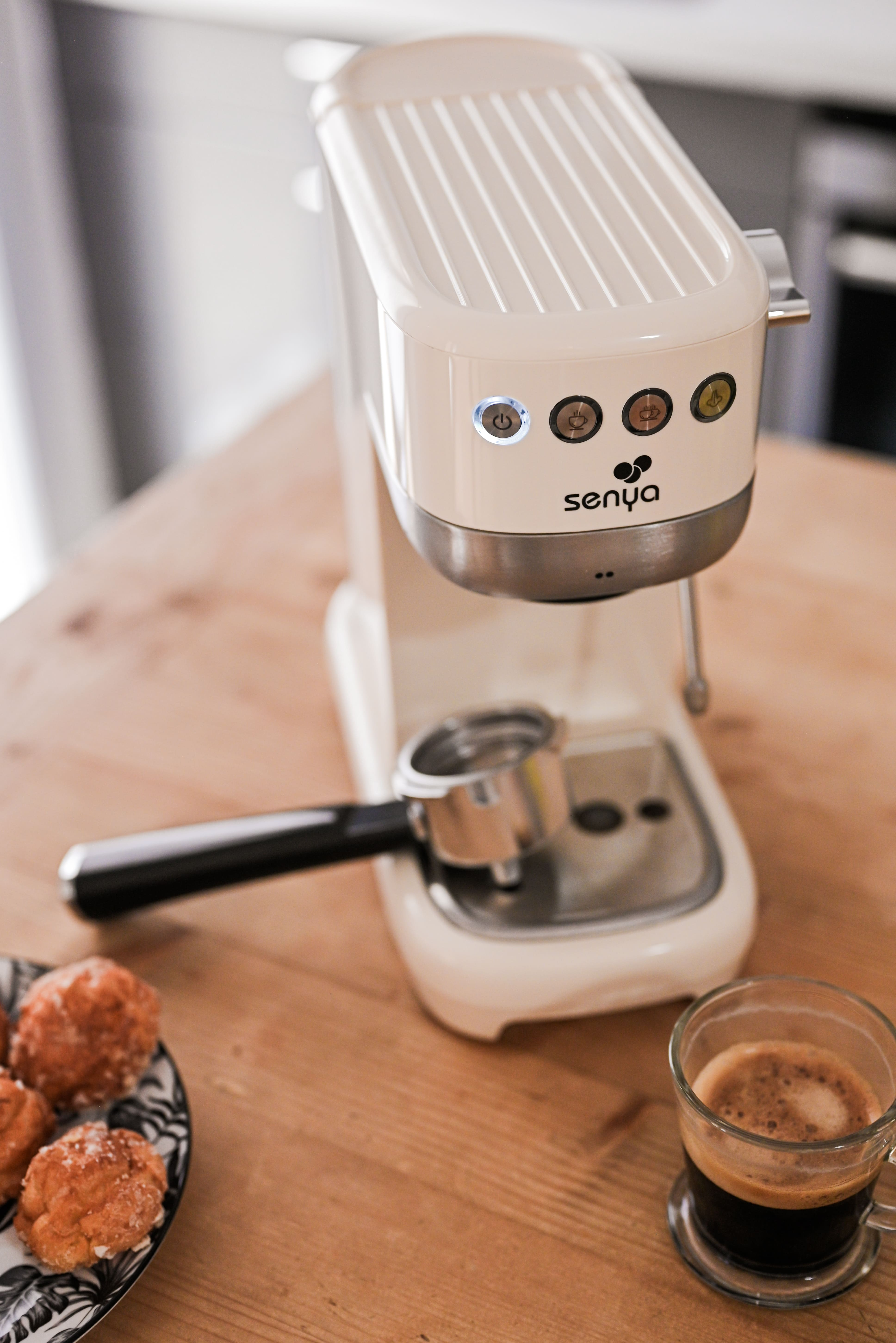 Creme Espressomaschine mit Siebträger, Kaffee und Gebäck auf einem Holztisch.
