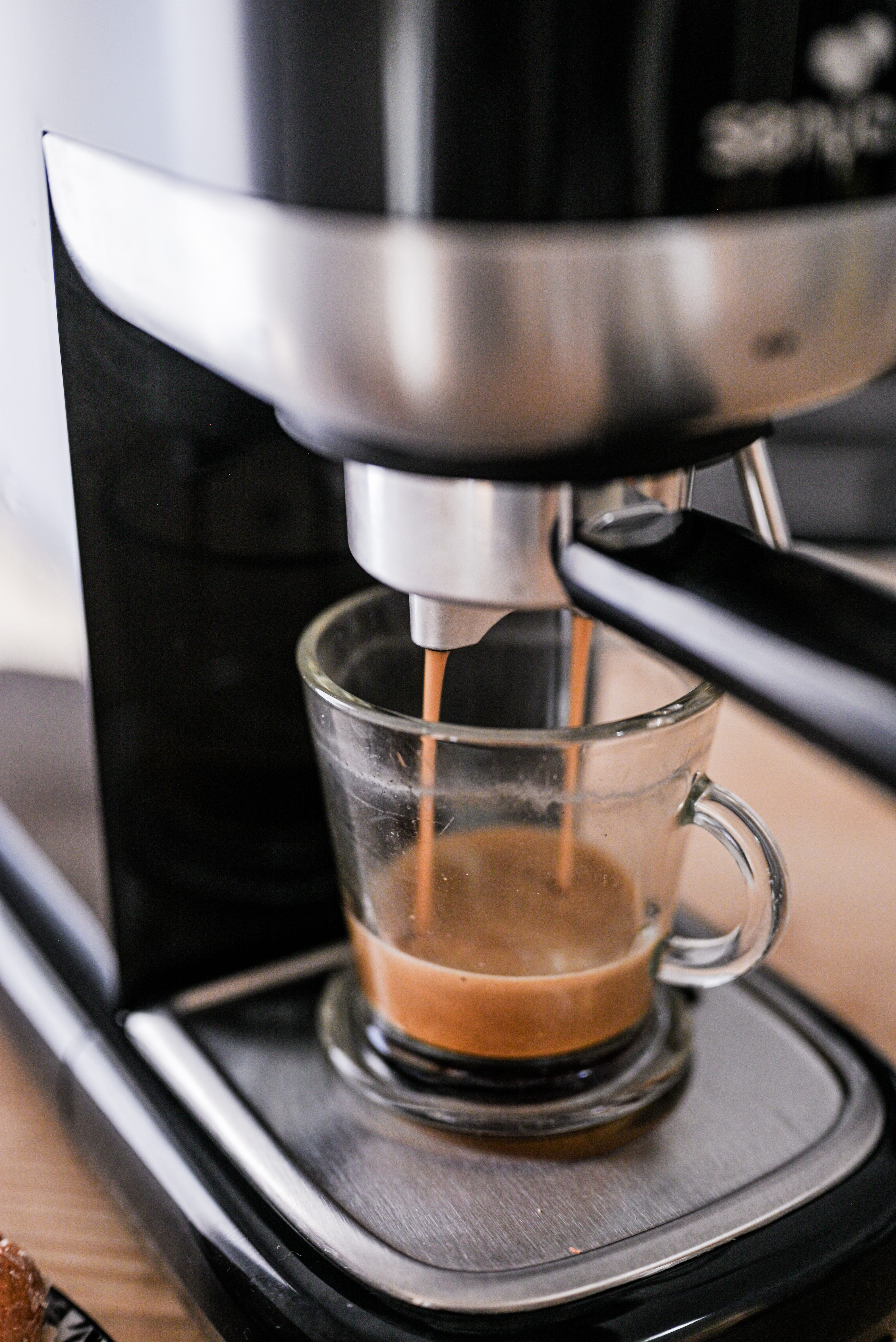 Espressomaschine gießt Kaffee in eine Glastasse auf einem Metalltablett. Nahaufnahme.