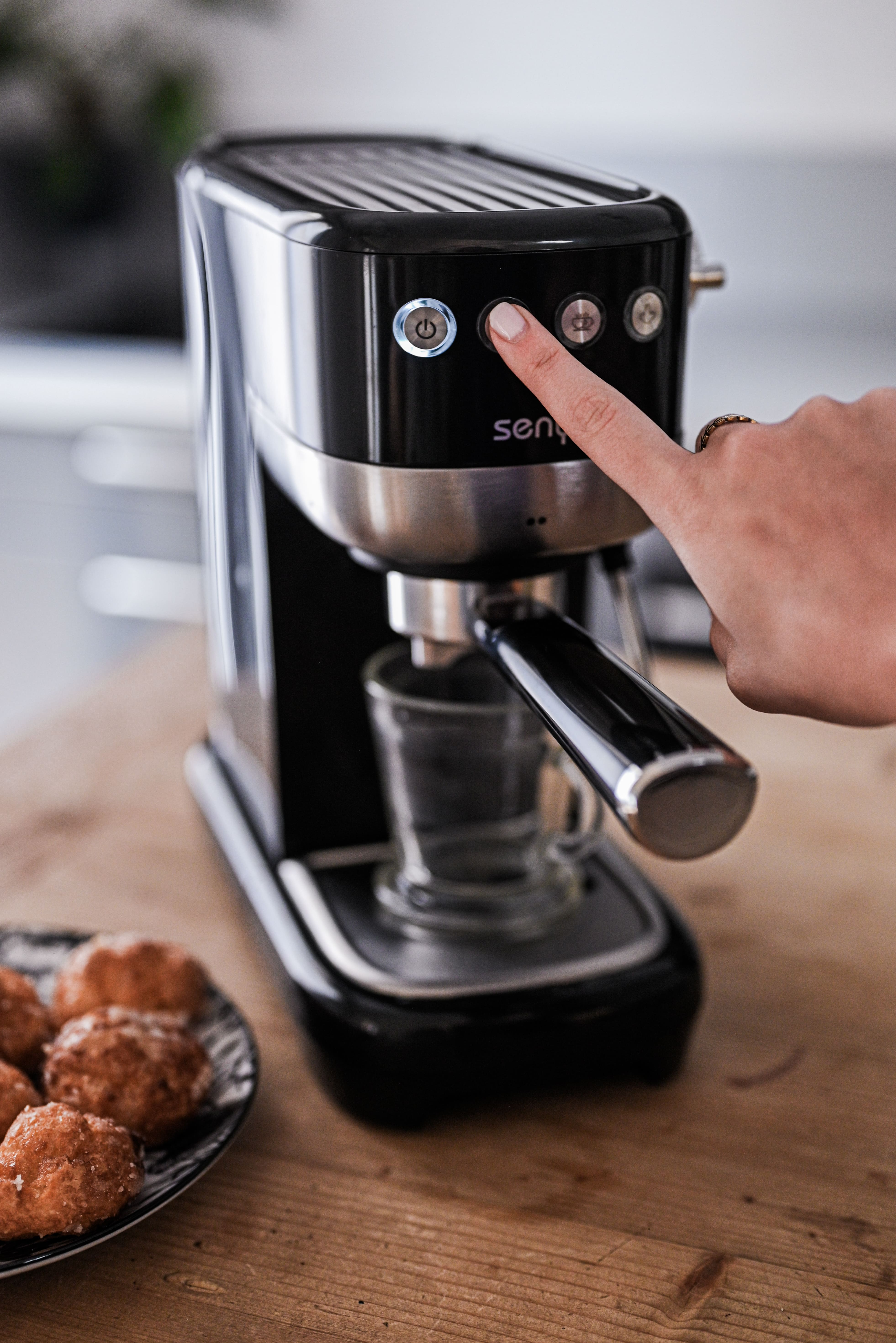 Die Hand einer Person drückt die Power-Taste einer schwarzen Espressomaschine.