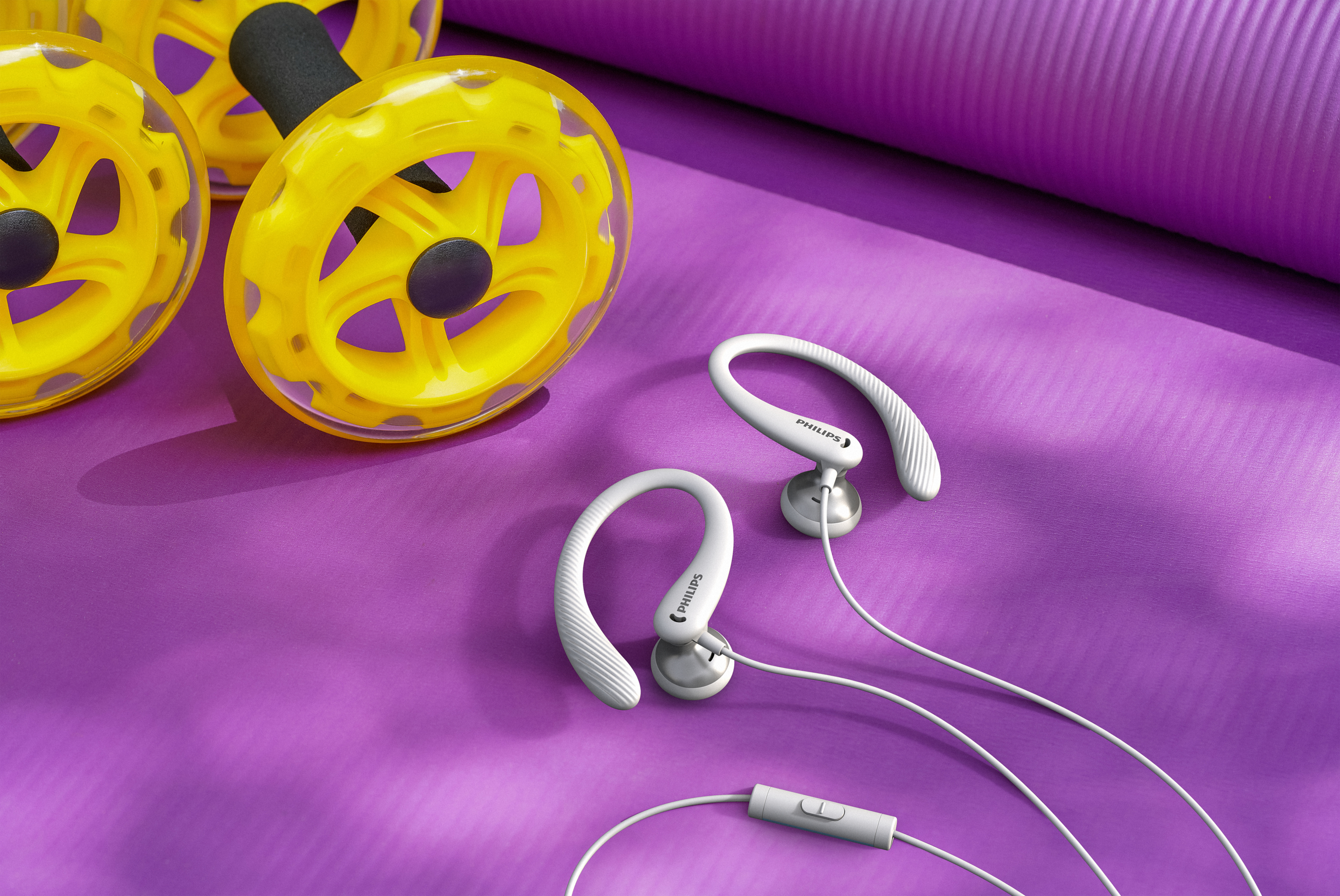 Białe sportowe słuchawki i żółte kółka do ćwiczeń na fioletowej macie do jogi. Kontekst fitness.