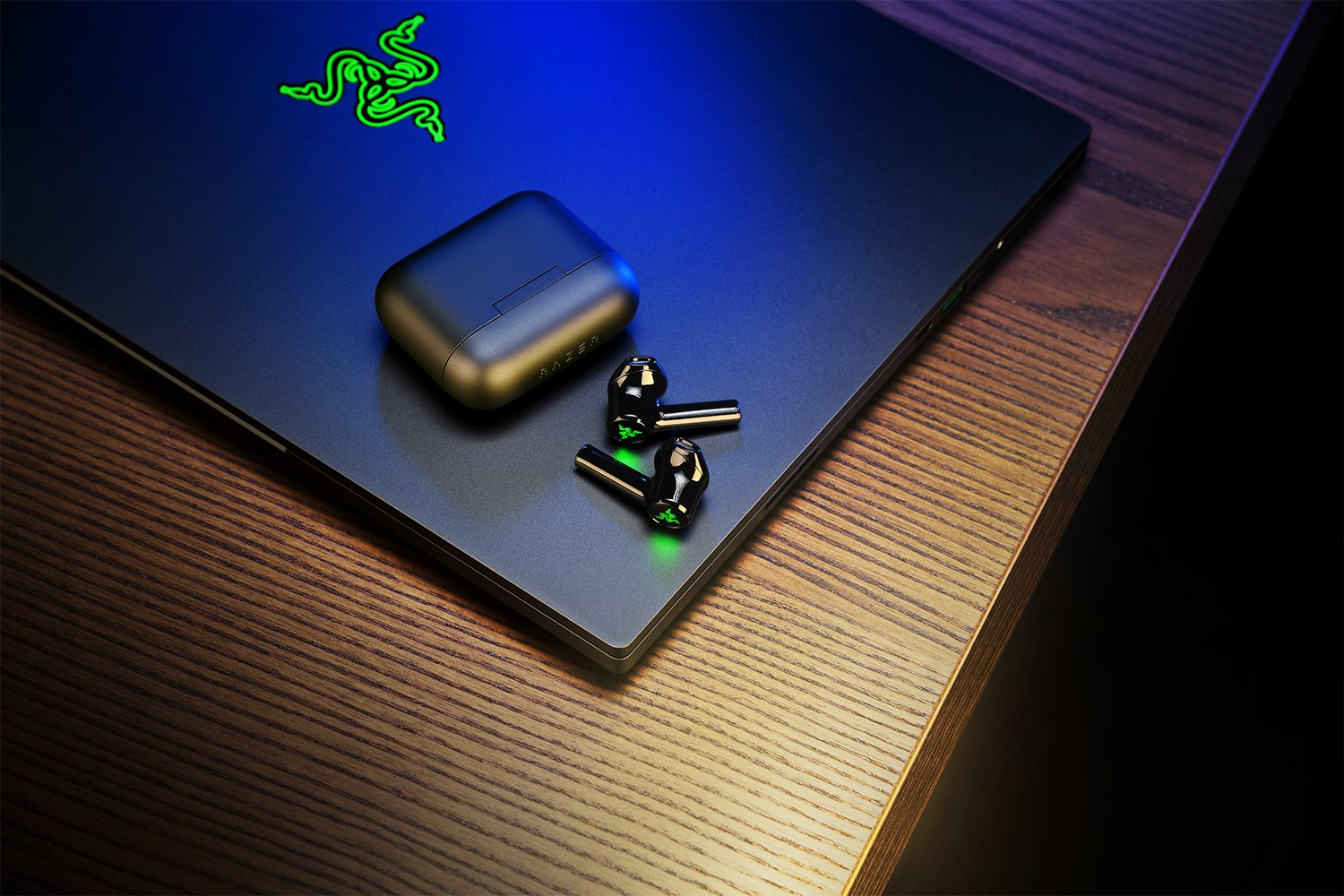 Czarny laptop Razer ze słuchawkami i etui na drewnianym stole.