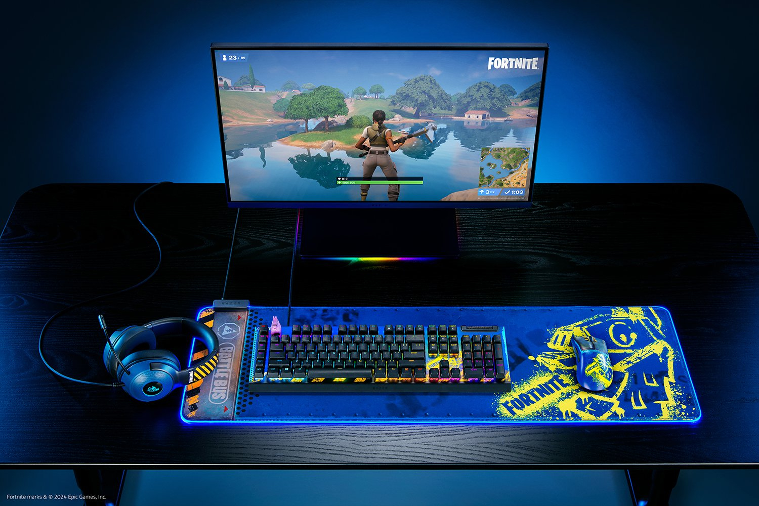 Konfiguracja do gier z monitorem pokazującym Fortnite, klawiaturą, myszą i zestawem słuchawkowym na niebieskiej podkładce.