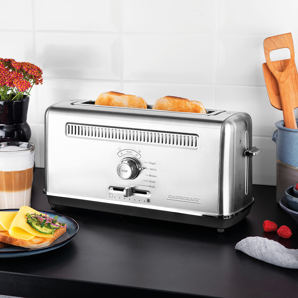 Srebrny toster z dwoma kromkami tostowanego chleba. Inne produkty spożywcze na blacie.