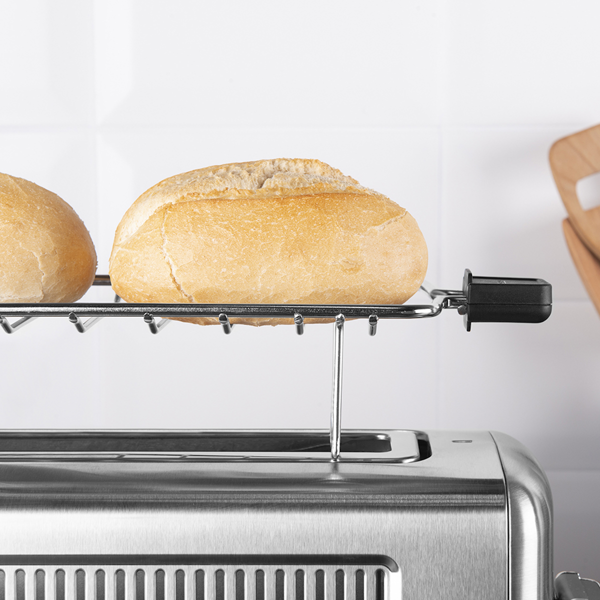 Dwie bułki na srebrnym ruszcie nad tosterem. Białe kafelkowe tło.