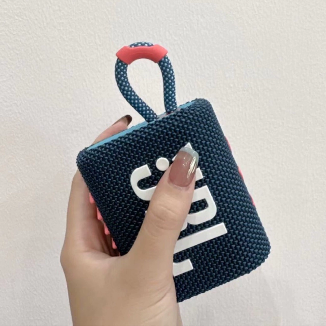 Hand hält einen kleinen blauen und marinefarbenen JBL-Lautsprecher mit rotem Griff.