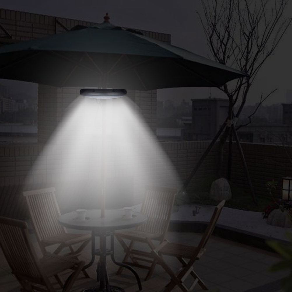 Ein beleuchteter Schirm mit Licht darüber, beleuchtet Sitzgelegenheiten im Freien bei Nacht. Dunkler Hintergrund.