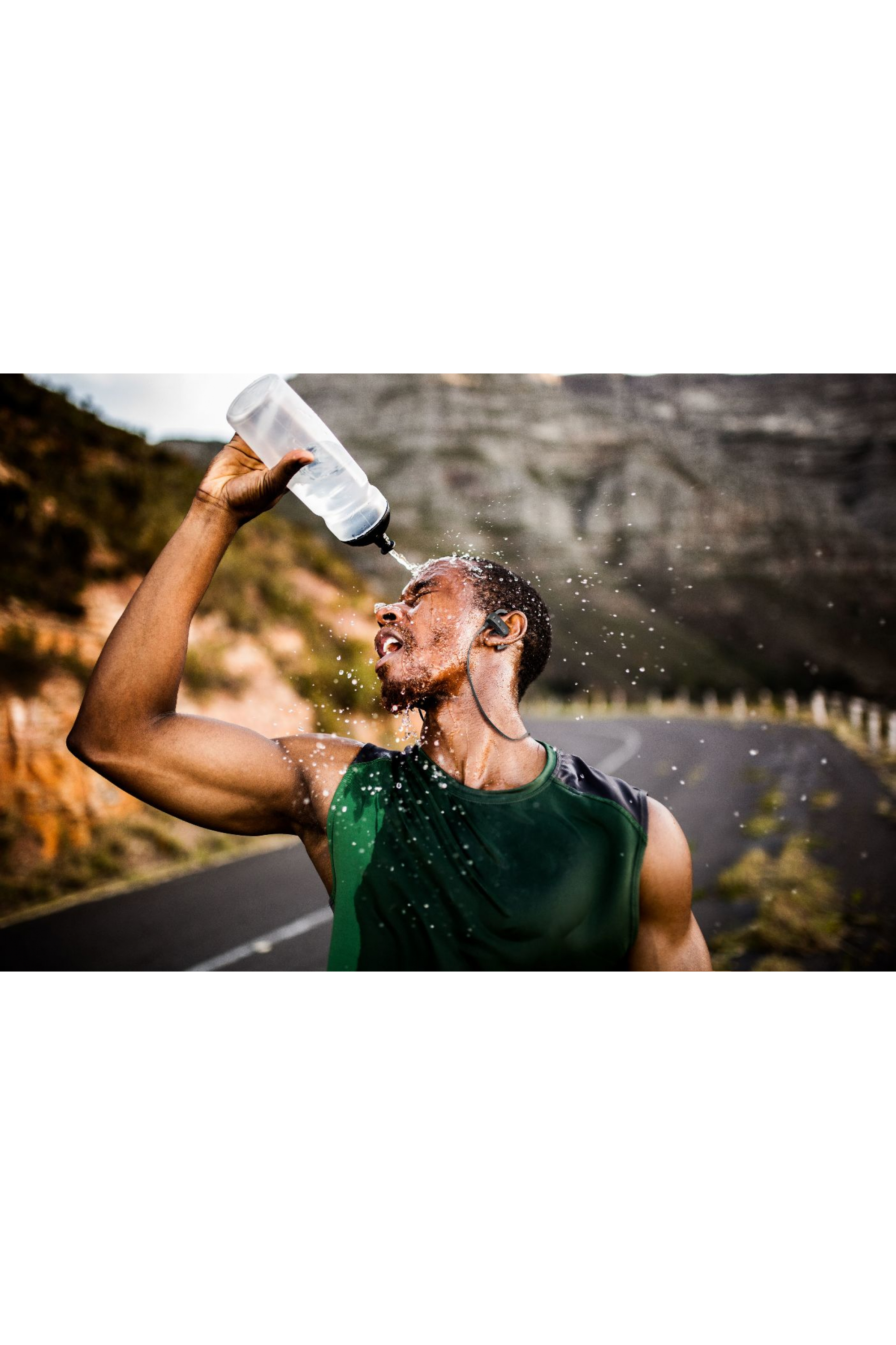 Mężczyzna polewa głowę wodą. Biegnie drogą obok góry.