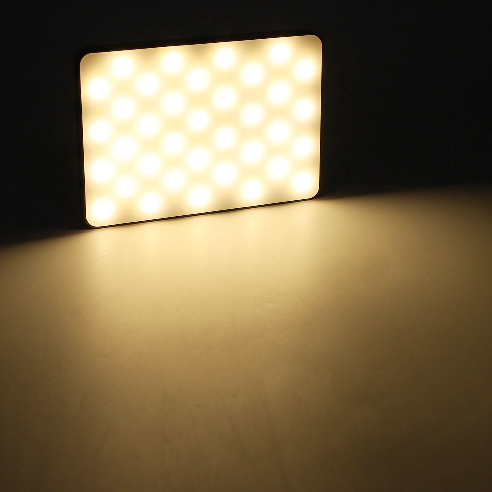 Ein quadratisches LED-Lichtpanel mit warmweißen Lichtern, das einen Schatten auf eine helle Oberfläche wirft.