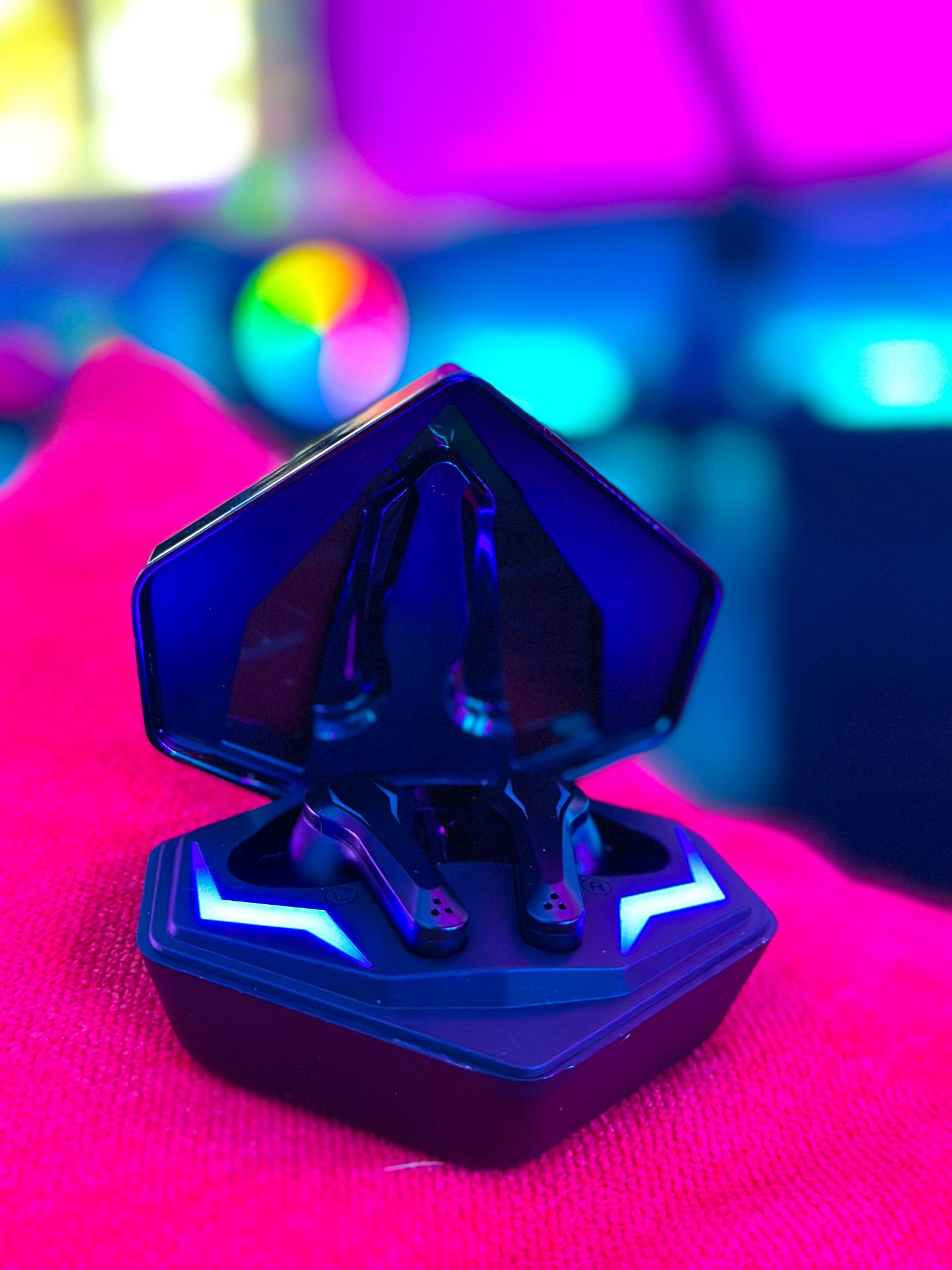 Czarne, otwarte etui na słuchawki z niebieskim i fioletowym światłem. Słuchawki widoczne, tło rozmyte.