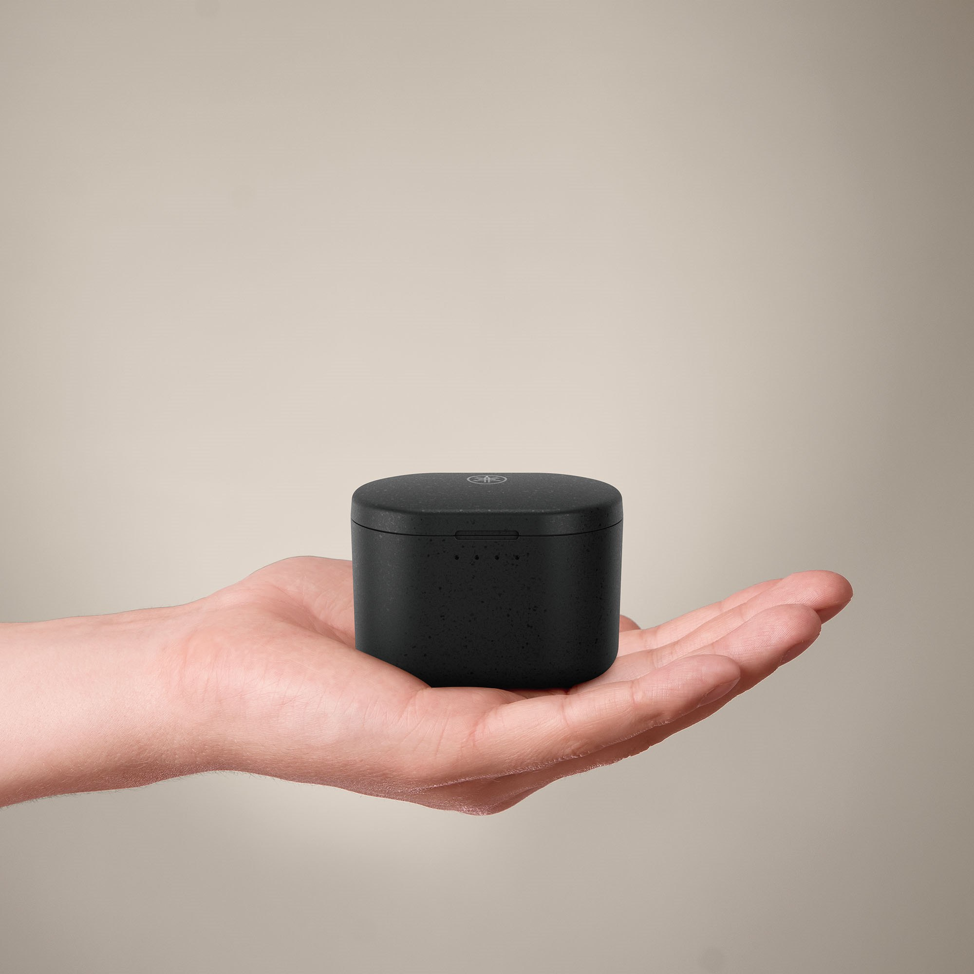 Dłoń trzymająca czarne, kwadratowe pudełko z zaokrąglonym wierzchem. Pudełko ma małe logo.