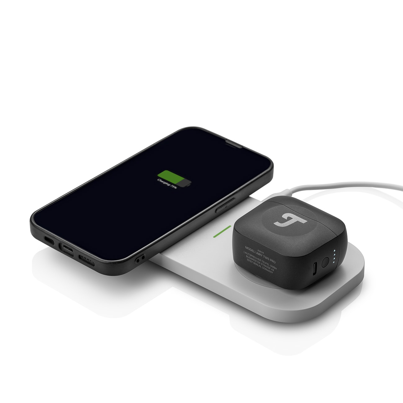 Czarny telefon na ładowarce bezprzewodowej z ładującymi się na niej słuchawkami. Białe tło.