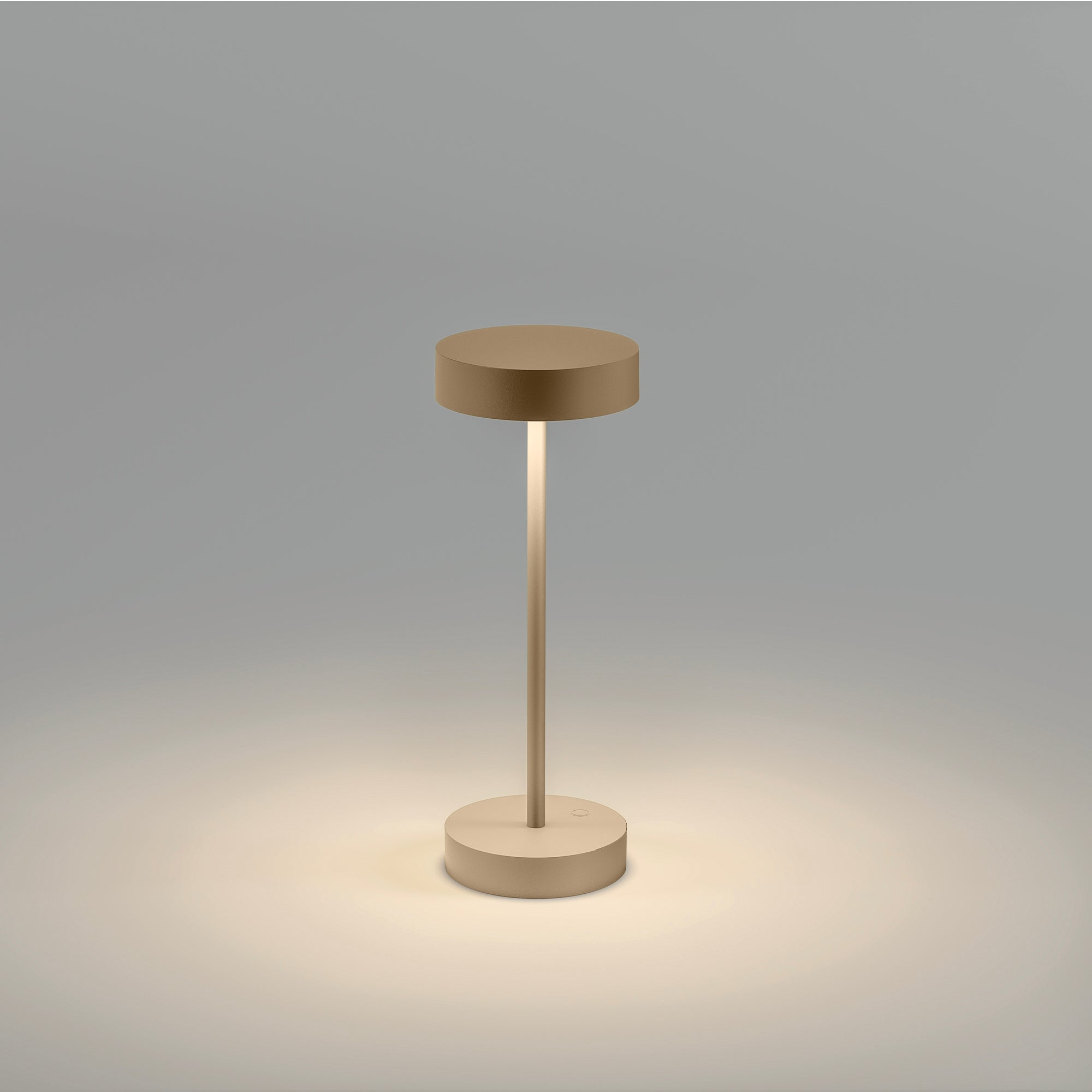 Eine kleine beige Tischlampe mit kreisförmigem Sockel und Oberteil sowie einem zentralen Schaft. Von unten beleuchtet.