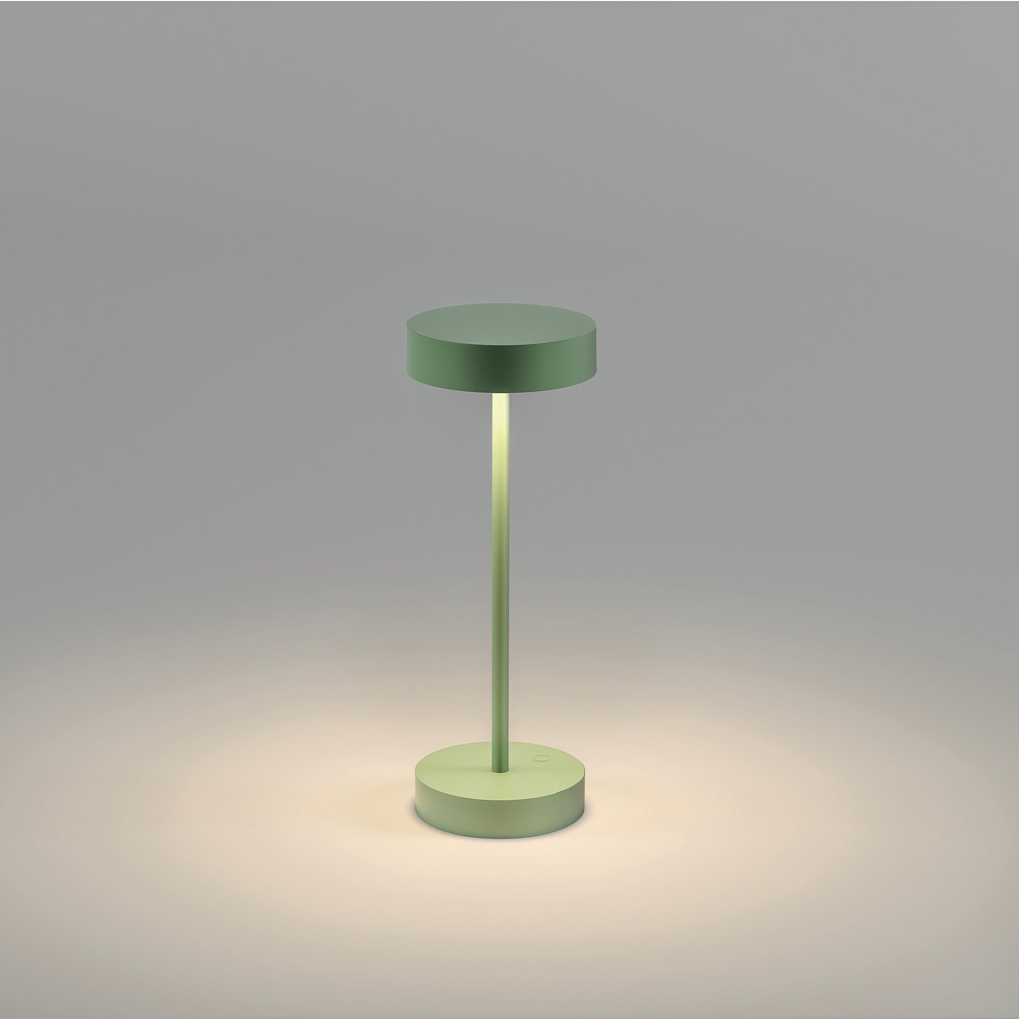 Grüne Tischlampe mit rundem Sockel und Oberteil, die Licht aussendet. Hellgrauer Hintergrund.