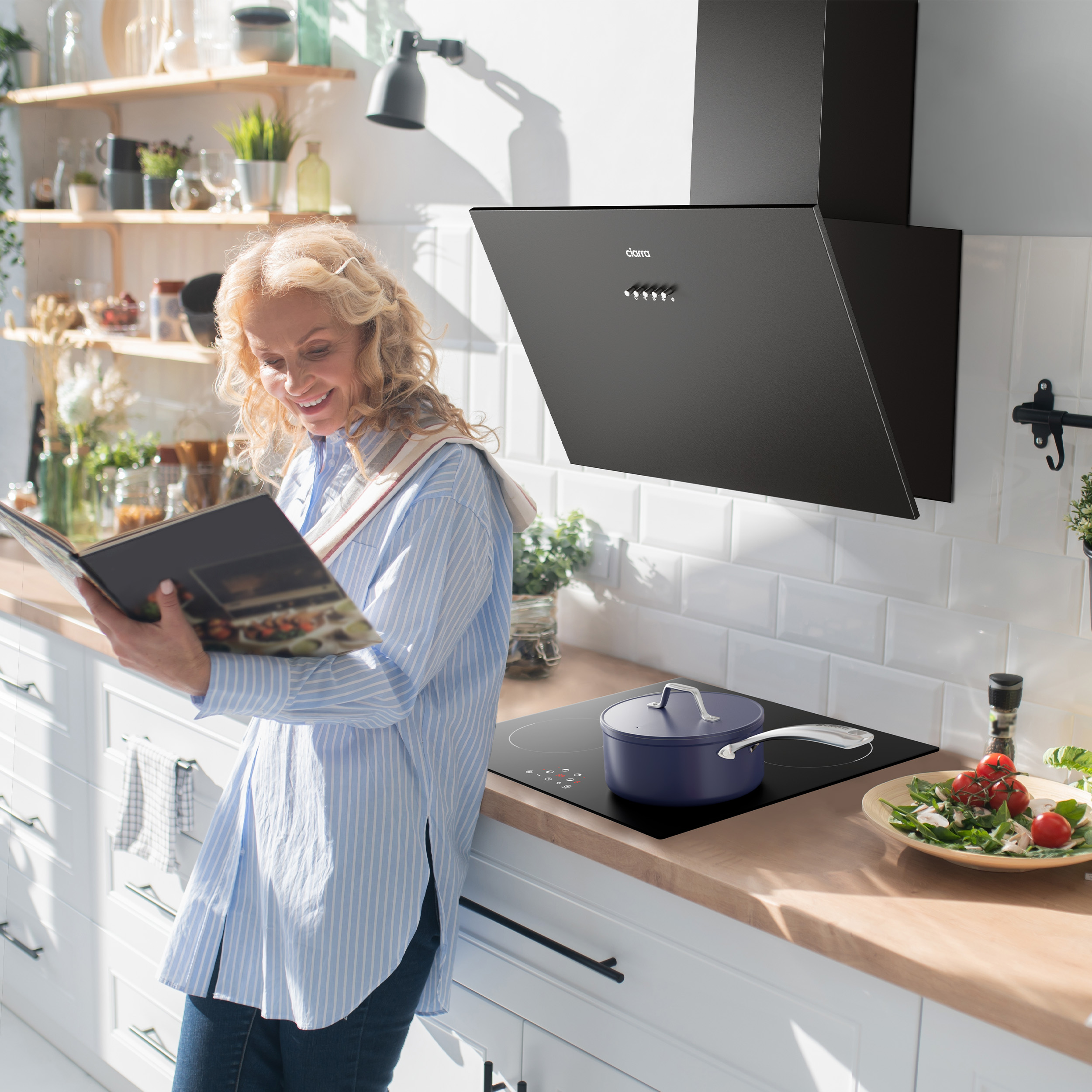 Vrouw in keuken, leest een kookboek, bij een zwarte afzuigkap en een fornuis.