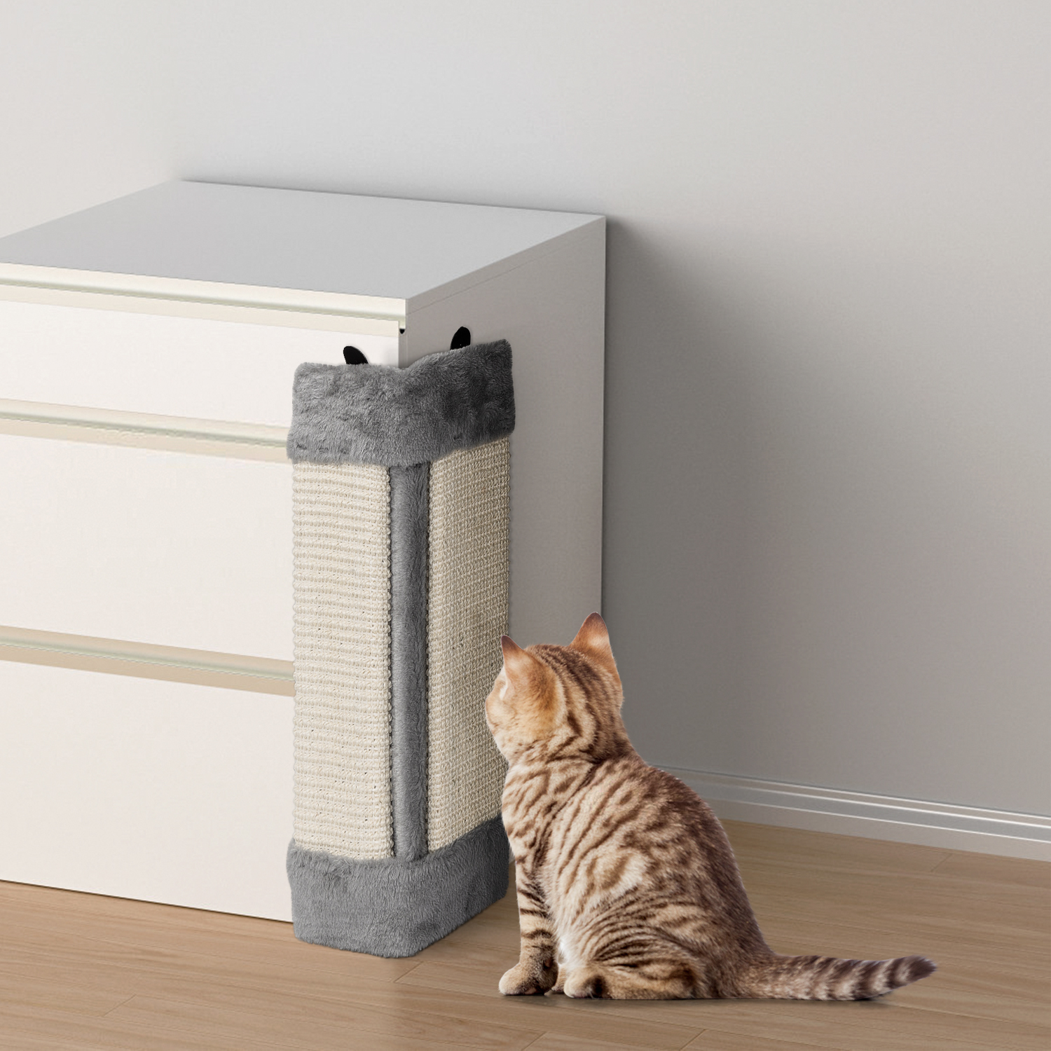 Un gato mirando un rascador de gatos adjunto a una cómoda blanca.