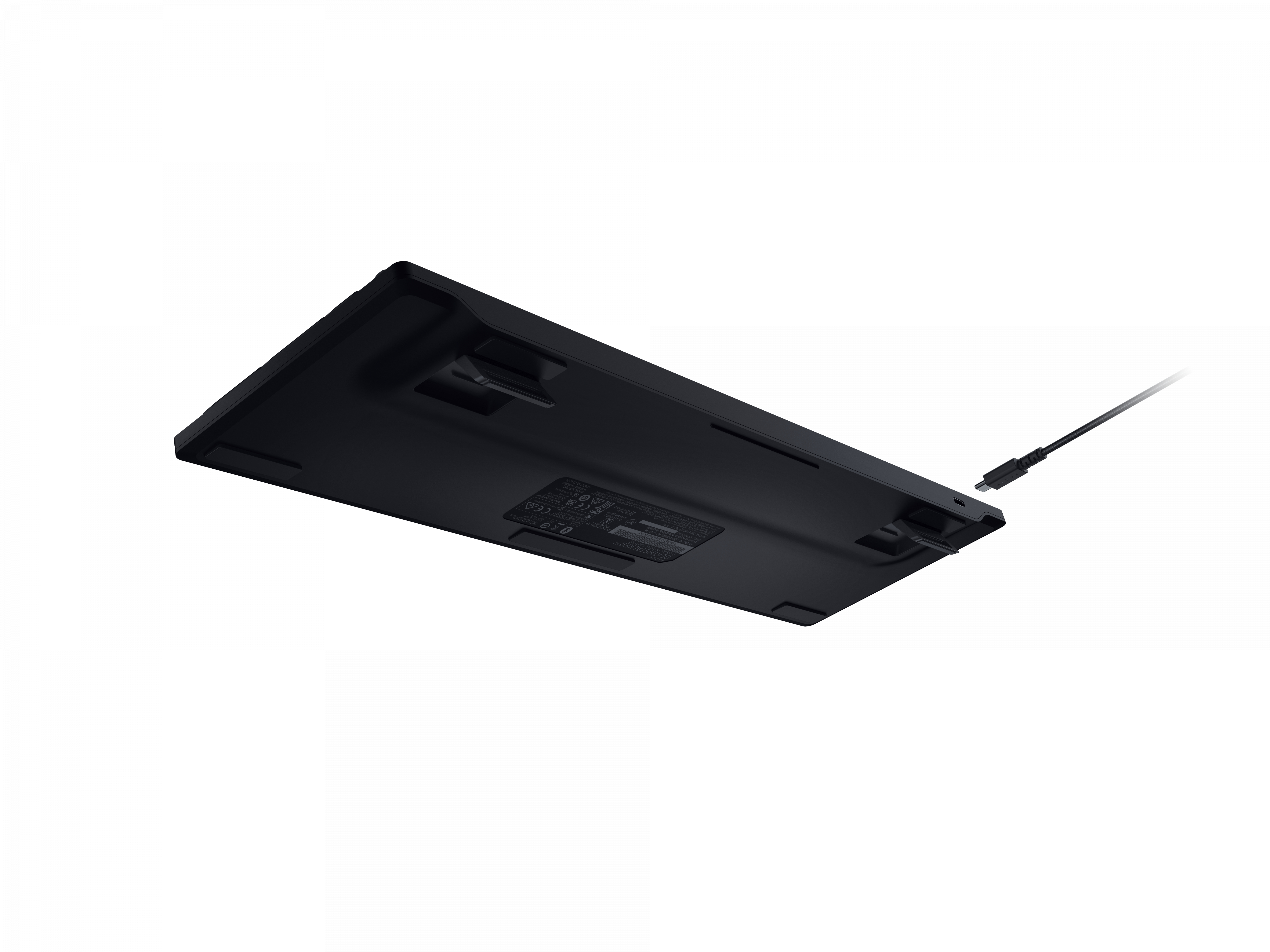 Spód czarnej klawiatury z wystającym kablem USB. Klawiatura leży na białej powierzchni.