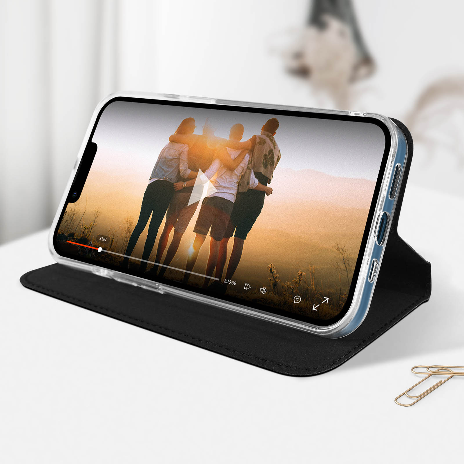 Smartphone con video in riproduzione, in custodia nera. Aperto su tavolo bianco, con graffetta.
