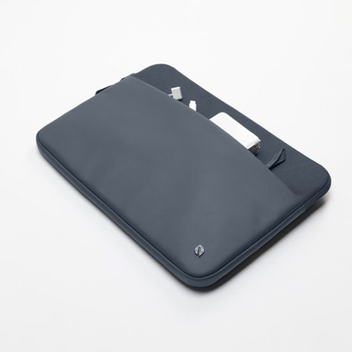 Una custodia per laptop grigio scuro con una tasca aperta contenente accessori bianchi su una superficie bianca.