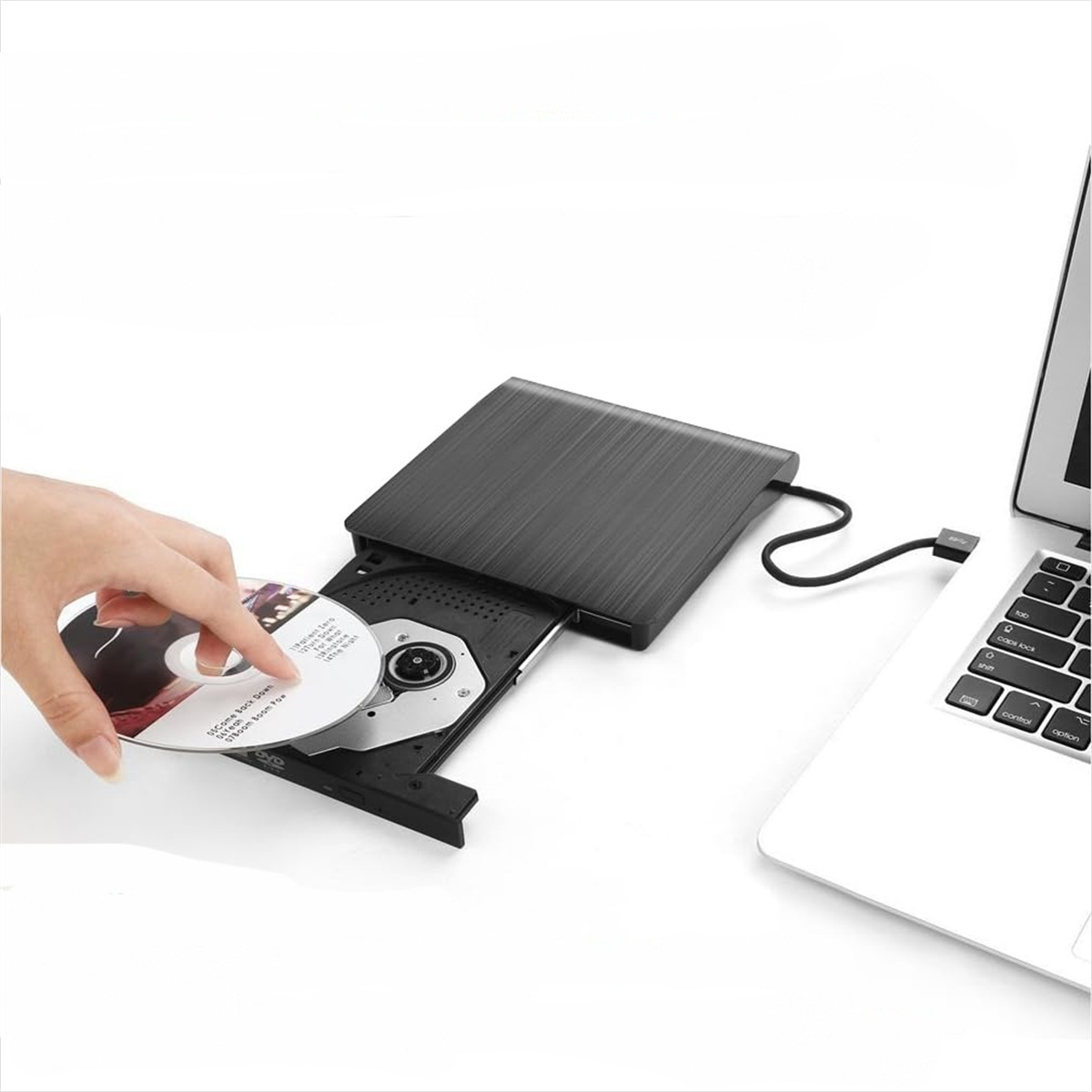 Eine Person legt eine CD in ein schwarzes externes CD/DVD-Laufwerk neben einem Laptop auf weißer Oberfläche ein.