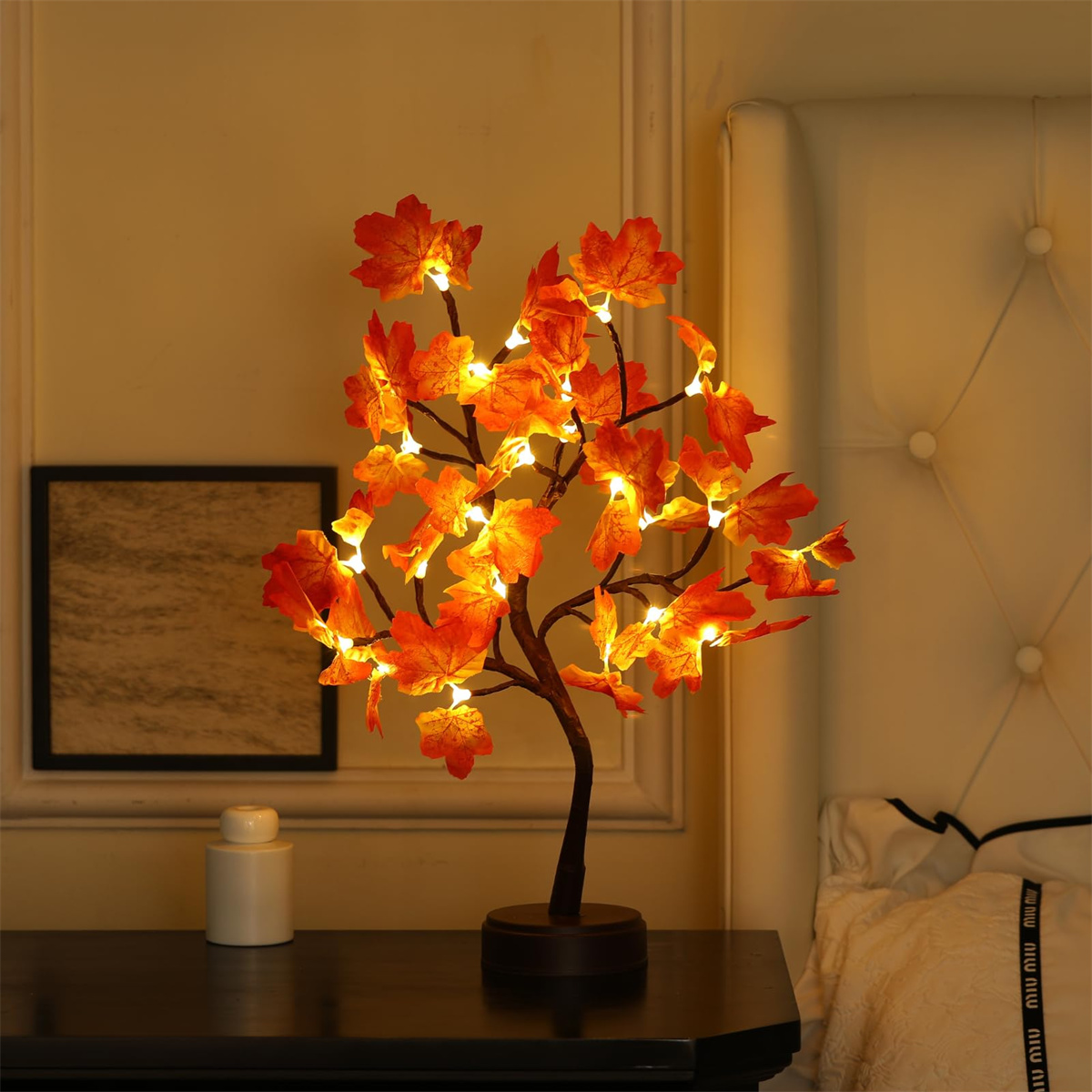 Eine kleine baumförmige Lampe mit orangefarbenen Ahornblattlichtern. Sie steht auf einer dunklen Oberfläche neben einer weißen Flasche.