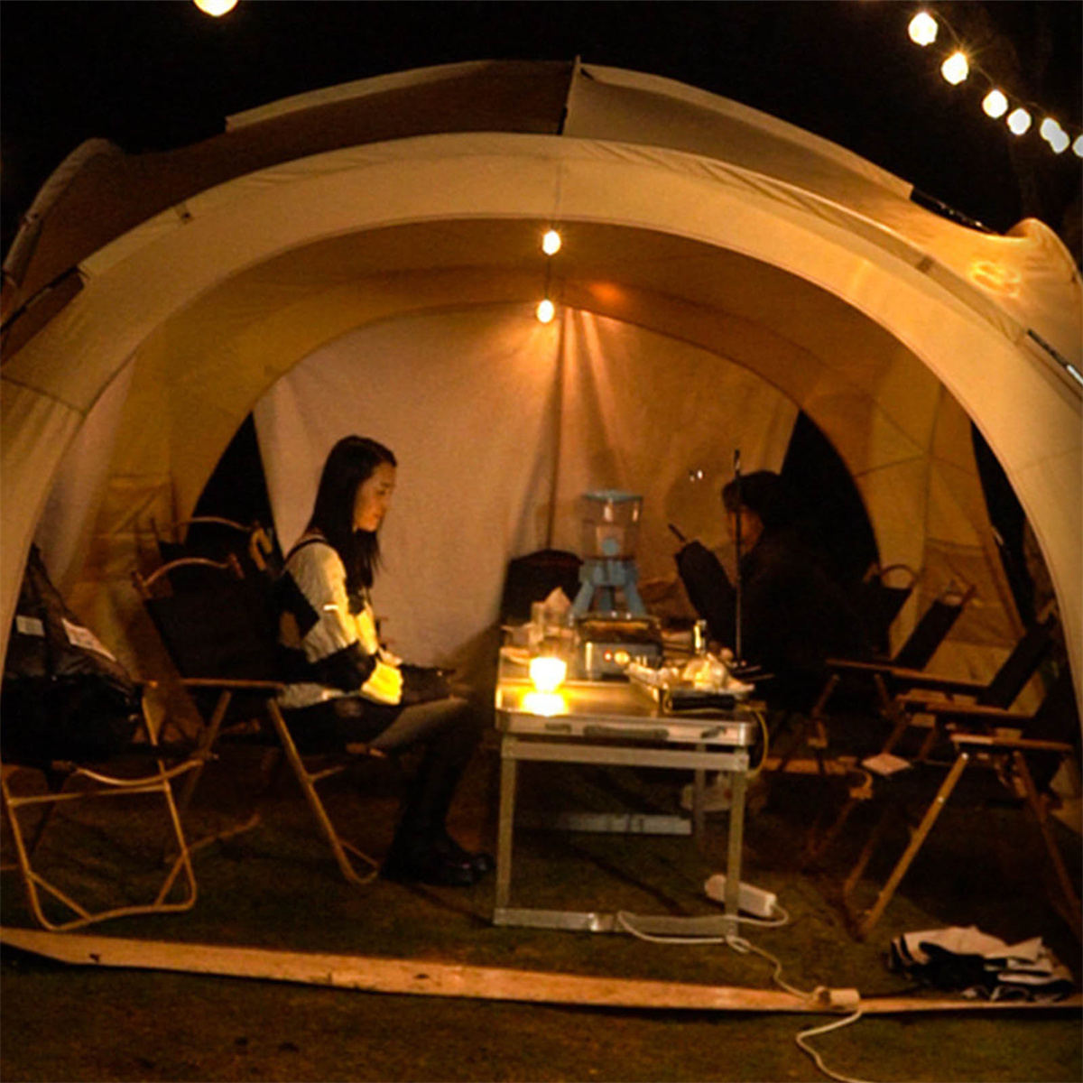 Zwei Personen in einem Zelt bei Nacht mit kleinem Tisch und Lichtern.