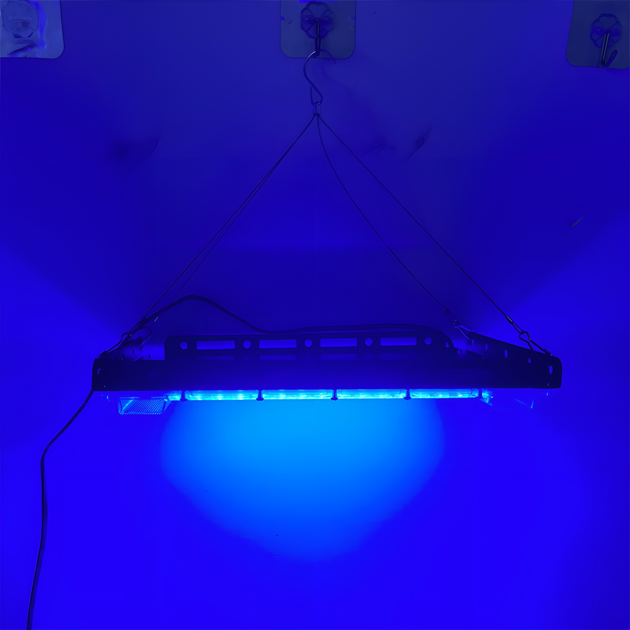 Blau beleuchtete, rechteckige Hängeleuchte vor weißer Wand.