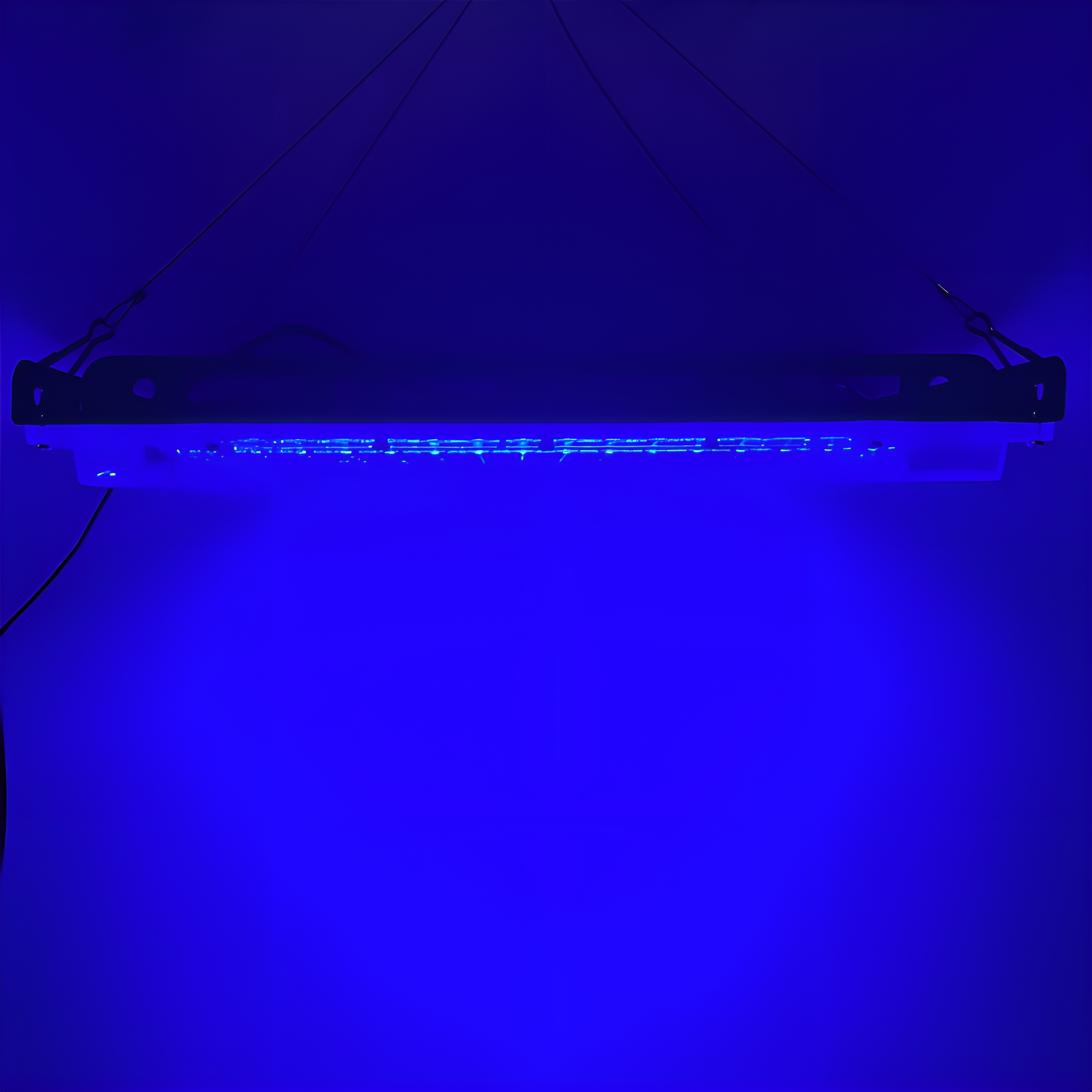 Lange, rechteckige blaue Lichtleiste, die an Drähten vor blauem Hintergrund hängt.