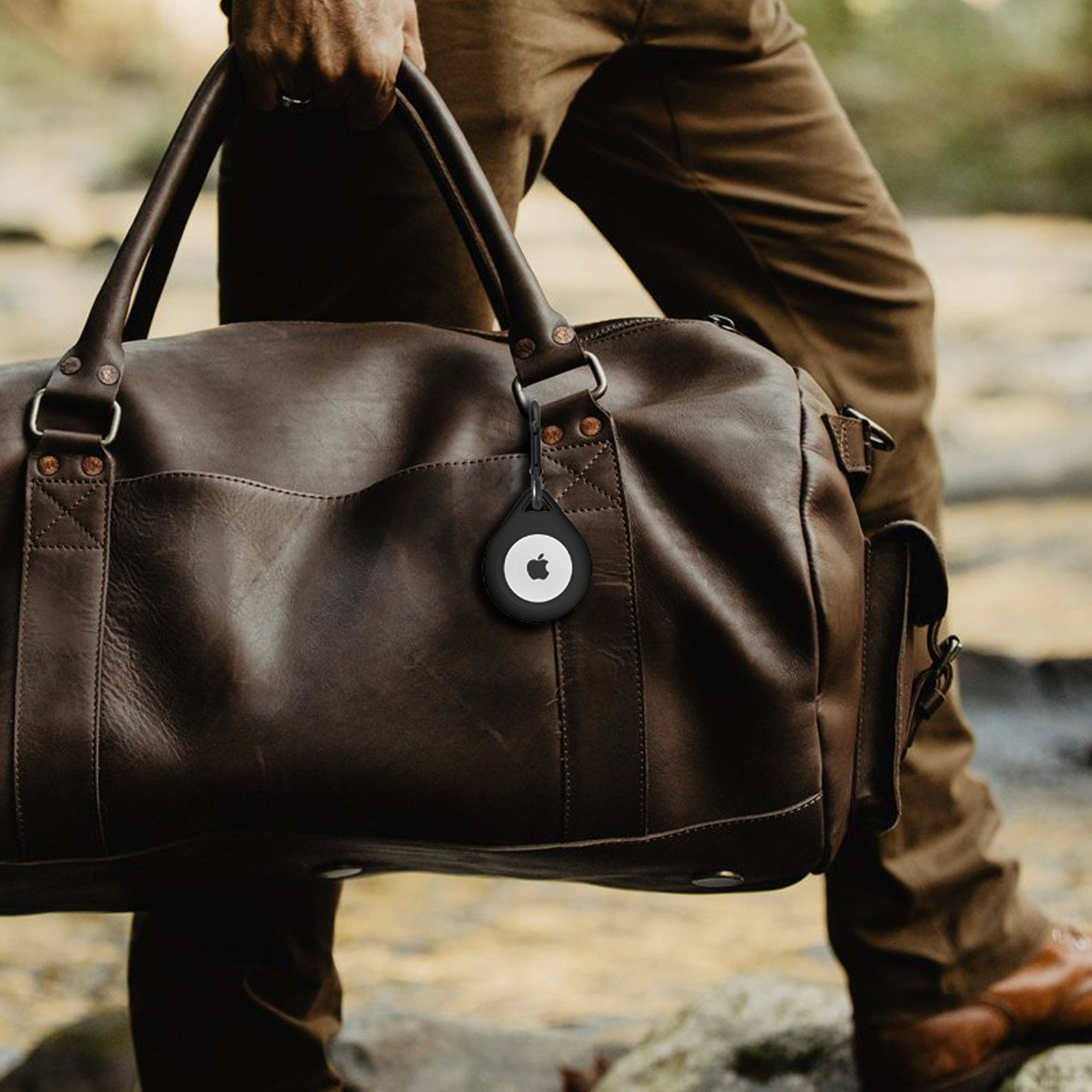 Person hält eine braune Tasche mit einem angebrachten schwarzen Anhänger.