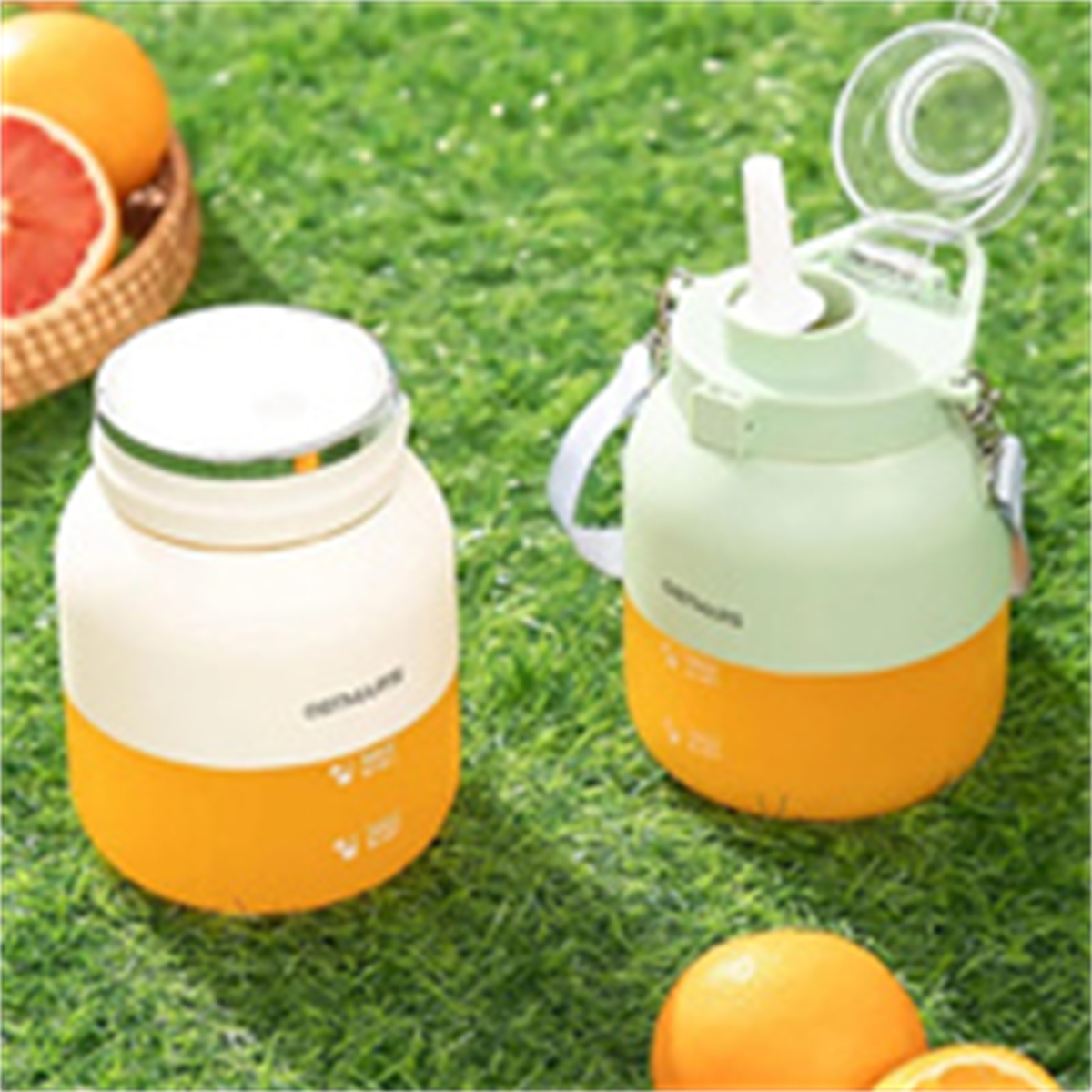 Zwei bunte Wasserflaschen auf Gras, mit Orangen im Hintergrund.