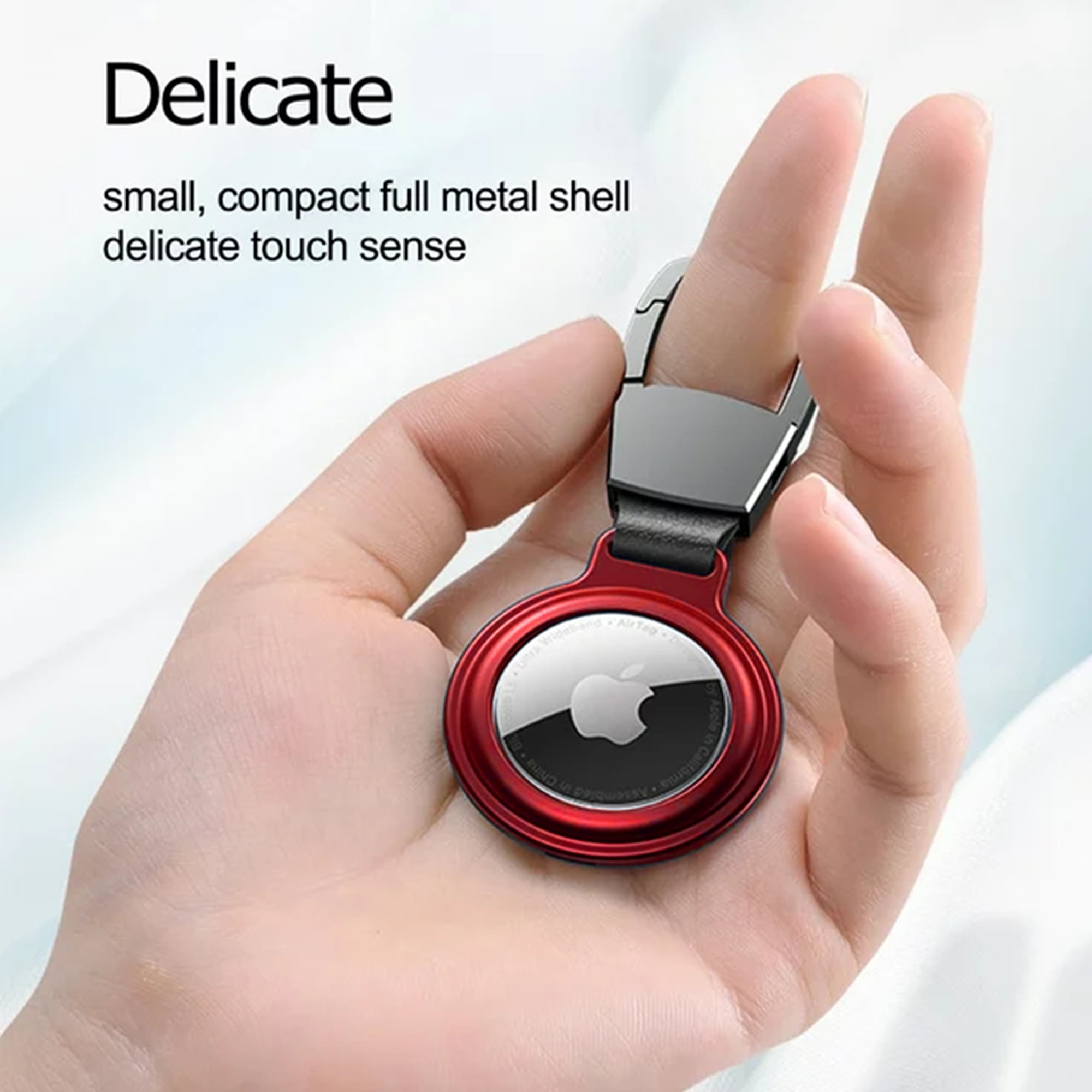 Ein rotes Apple AirTag in einem silbernen Metallhalter an einer Hand. Der Text betont die zarte Berührung.