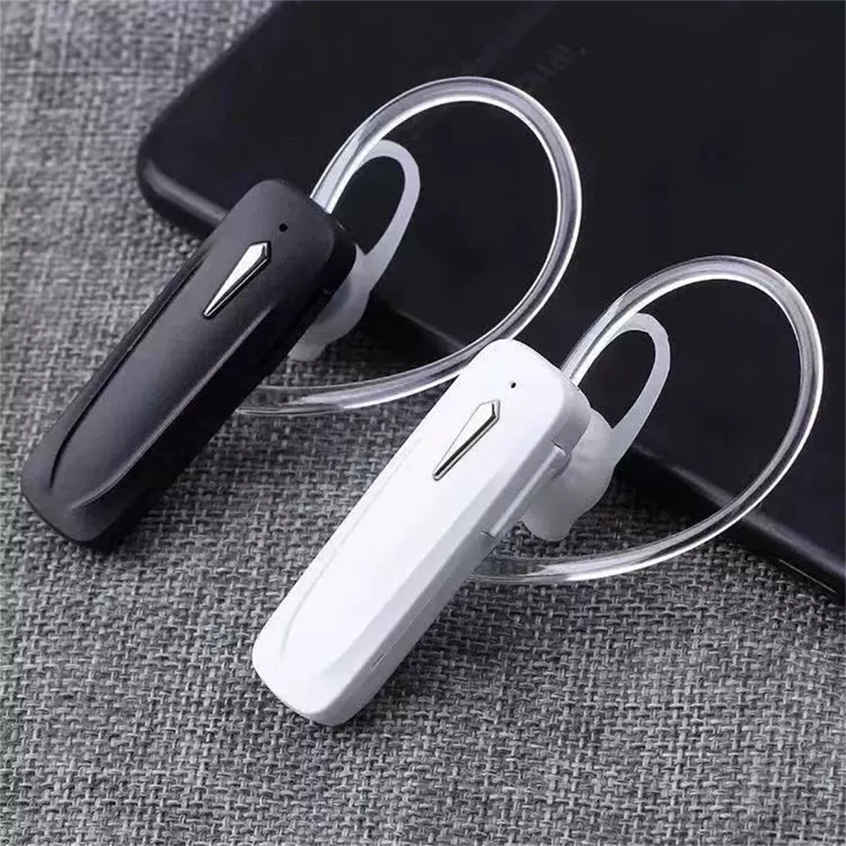 Zwei Bluetooth-Headsets, eines schwarz und eines weiß, liegen auf strukturierter Oberfläche.