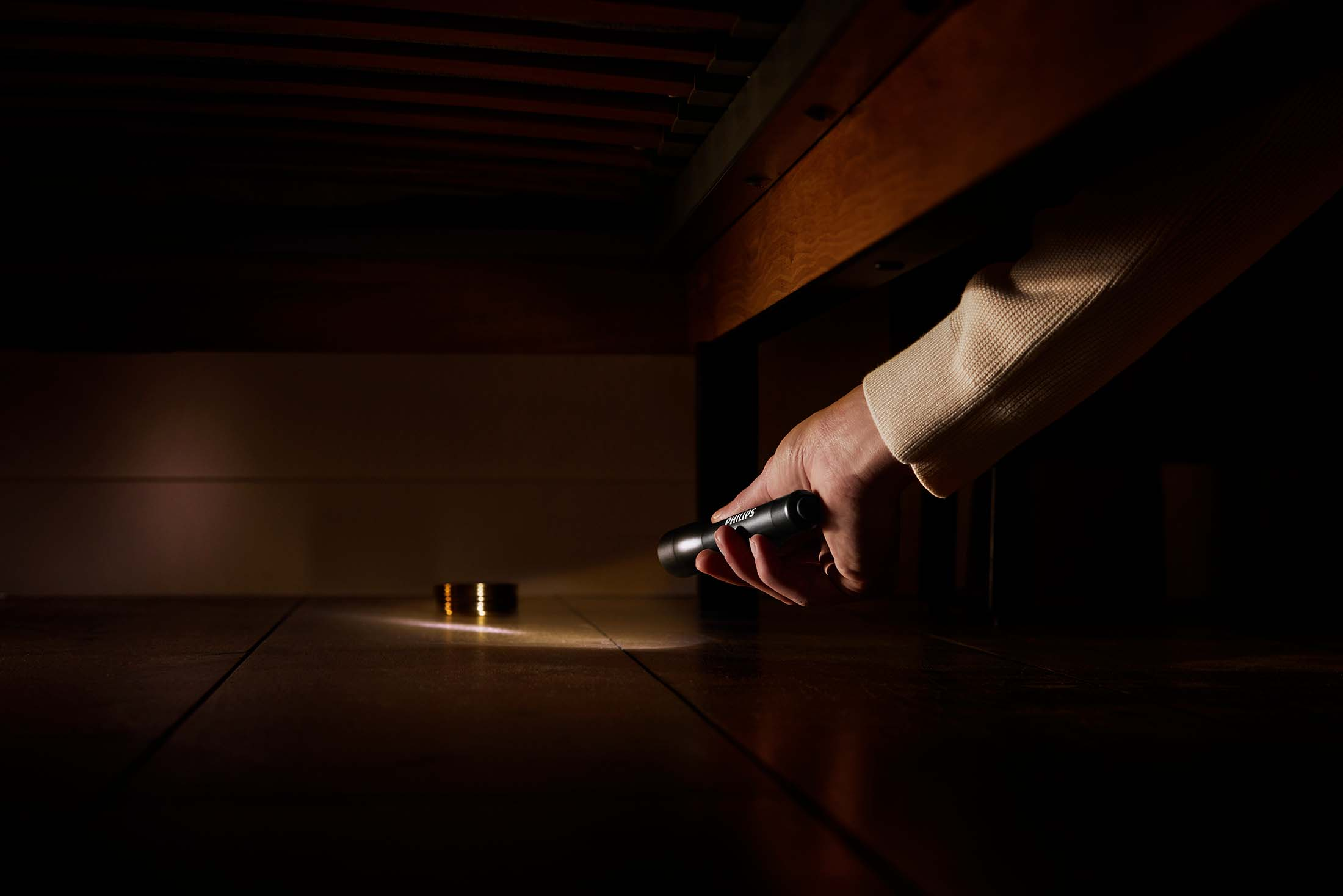 Una mano che tiene una torcia sotto un letto, illuminando il pavimento.
