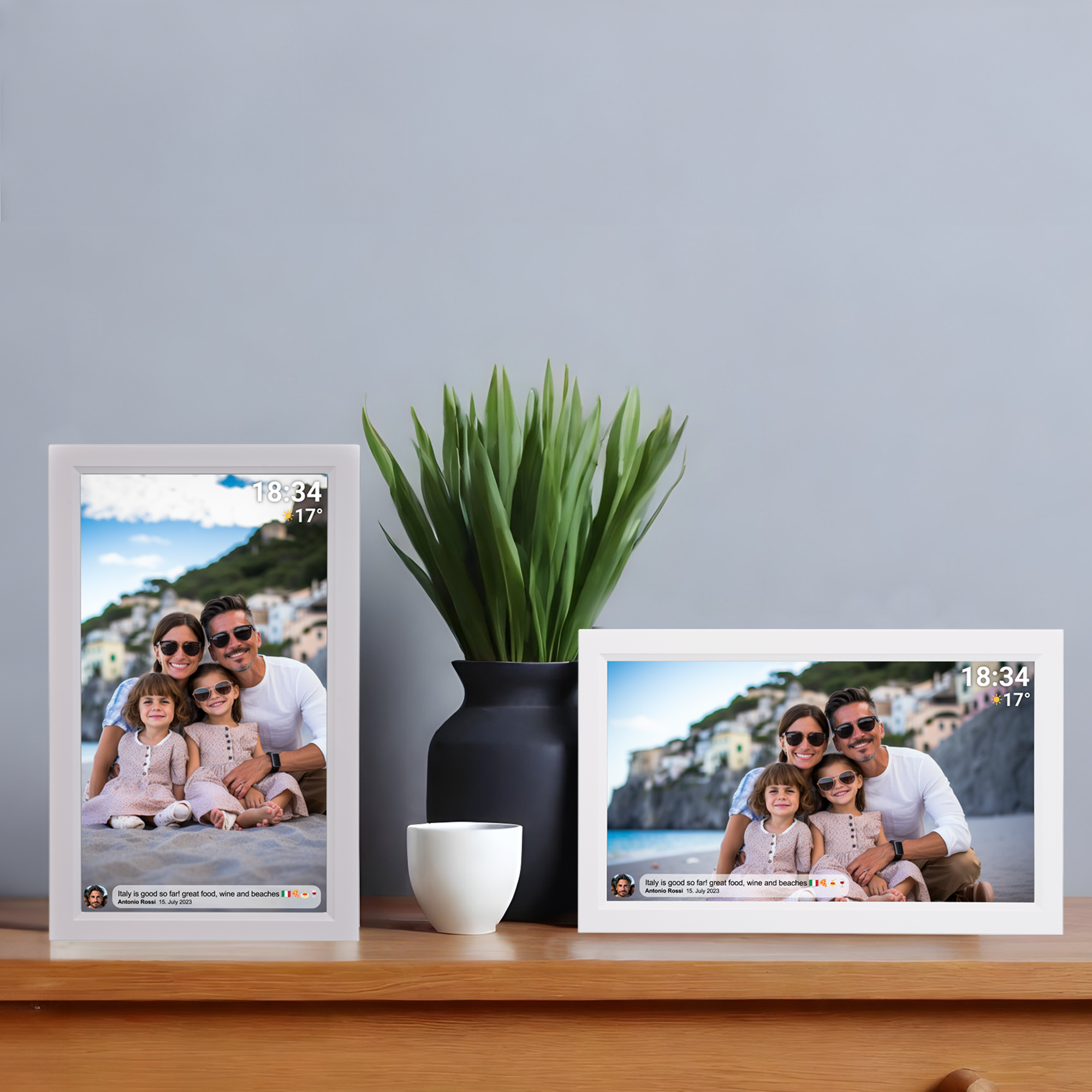 Deux cadres photo avec des photos de famille sur une table en bois, à côté d'un vase noir et d'une tasse blanche.