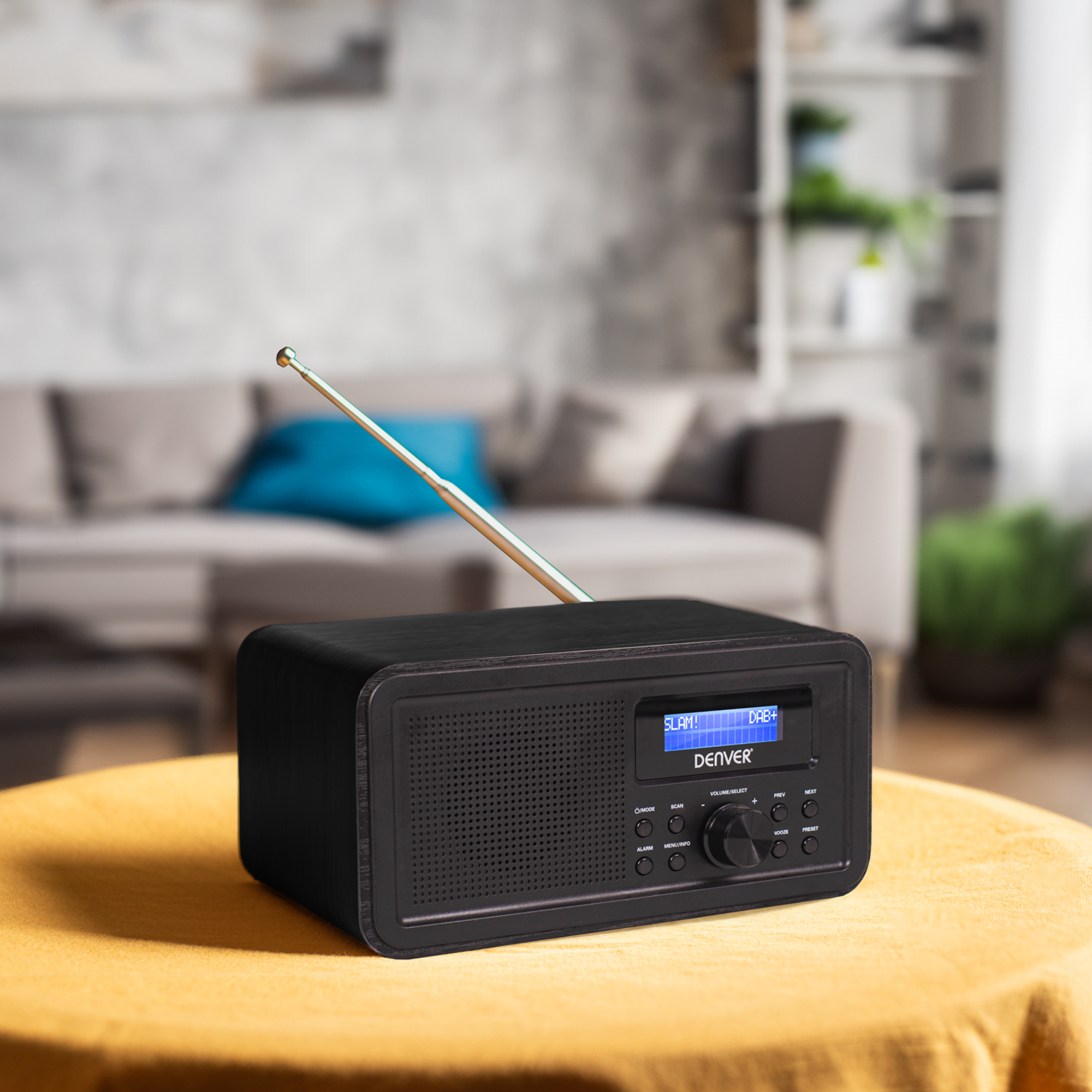 Czarny radio retro ze srebrną anteną, na żółtym stole, z rozmytym tłem.