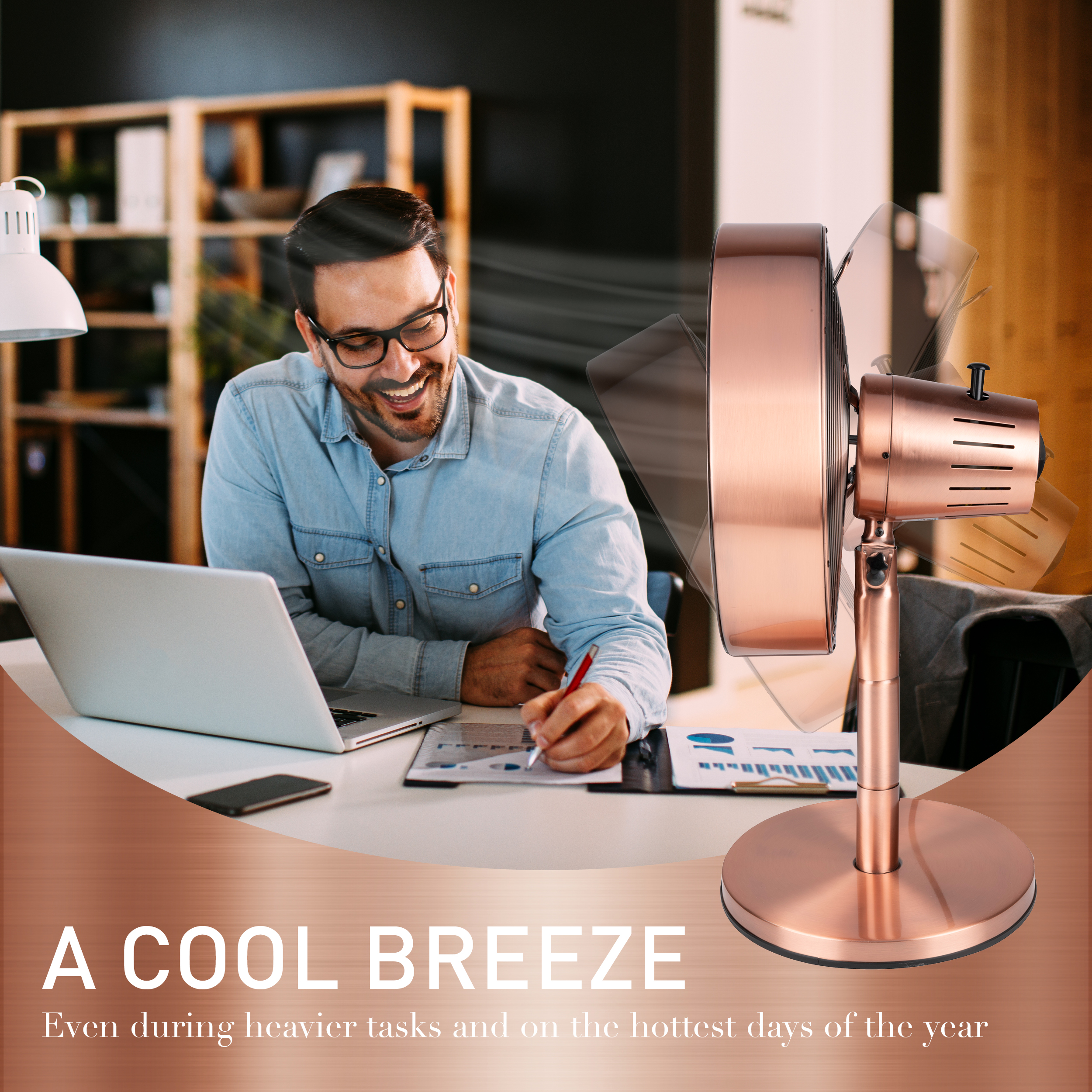 Un homme sourit en travaillant à son bureau. Un ventilateur en cuivre est au premier plan.
