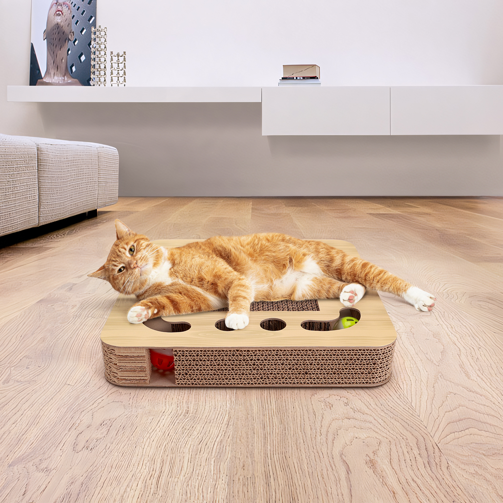 Un gato naranja y blanco descansando sobre un rascador de cartón con juguetes, en un piso de madera.