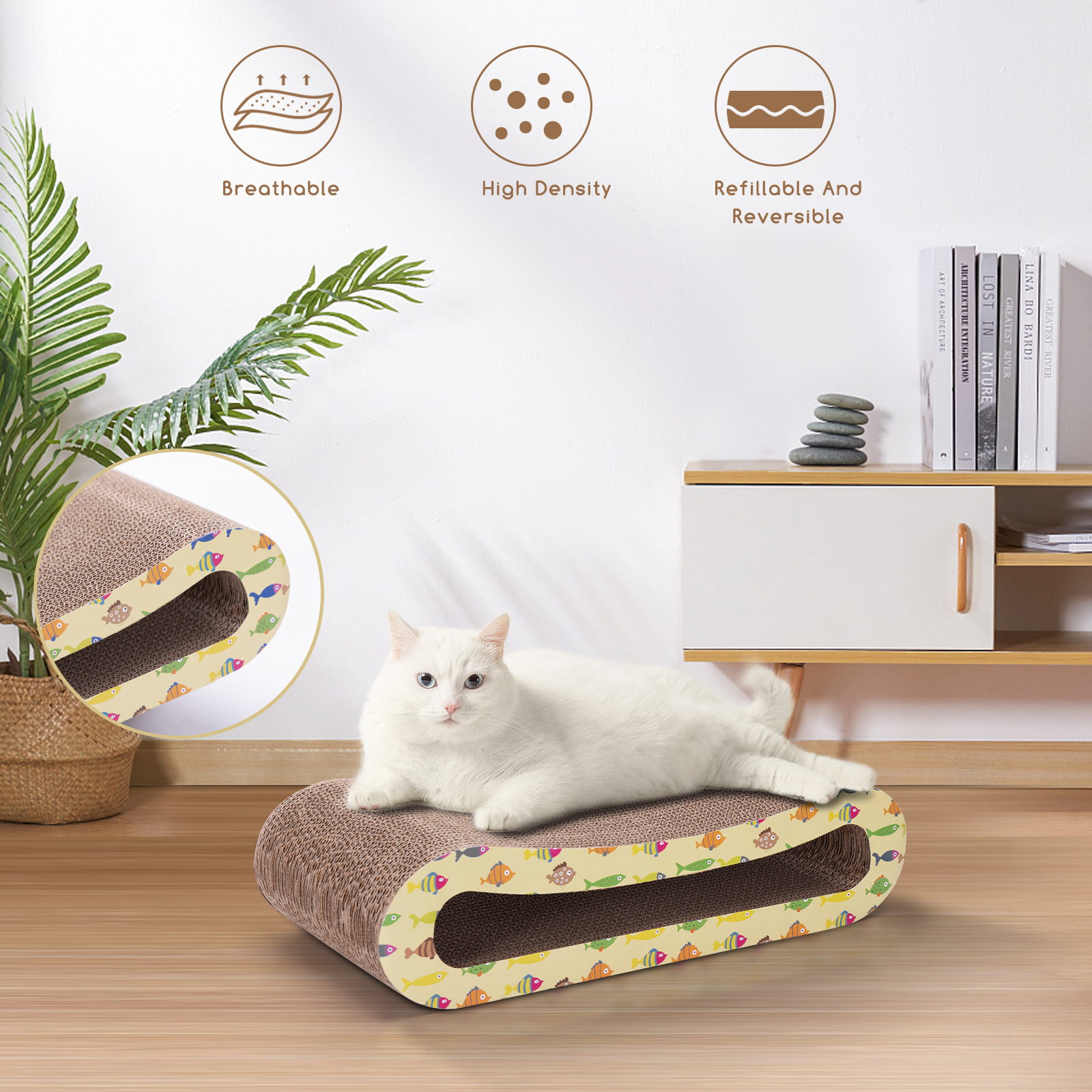Gato blanco en un rascador de cartón. El rascador tiene diseño de peces. Hay libros detrás.