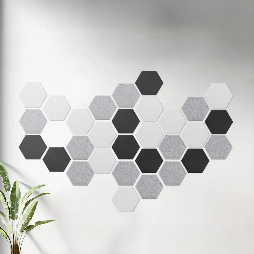 Una pared decorada con paneles hexagonales en blanco, gris y negro. Una planta en la esquina izquierda.